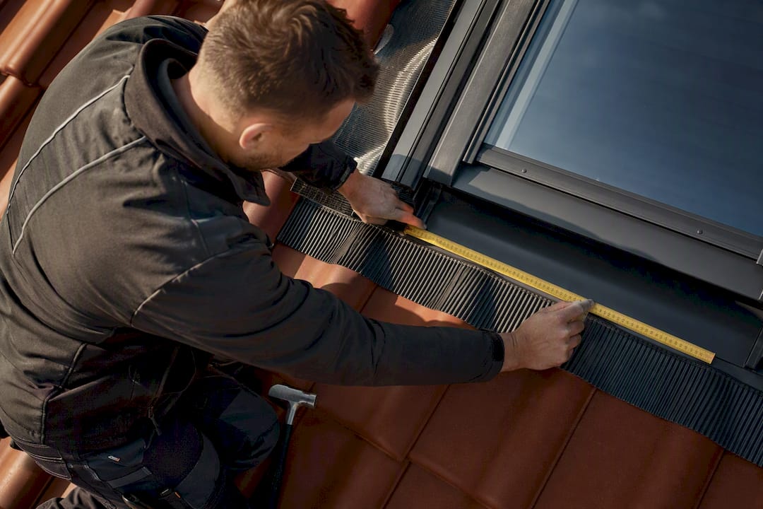 Dachdecker nimmt Maß am Dachfenster