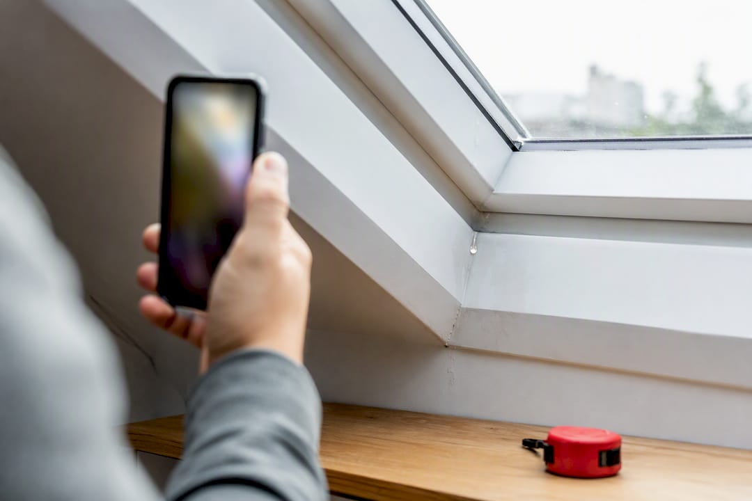Hand fotografiert die Tropfstelle am Dachfenster