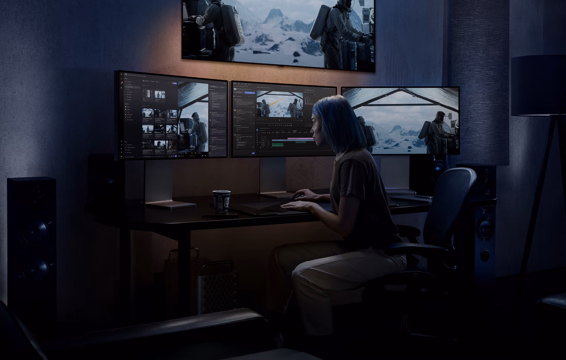 Une personne assise à un bureau sombre, travaillant sur un montage vidéo avec trois écrans affichant une scène de deux astronautes en milieu montagneux enneigé.