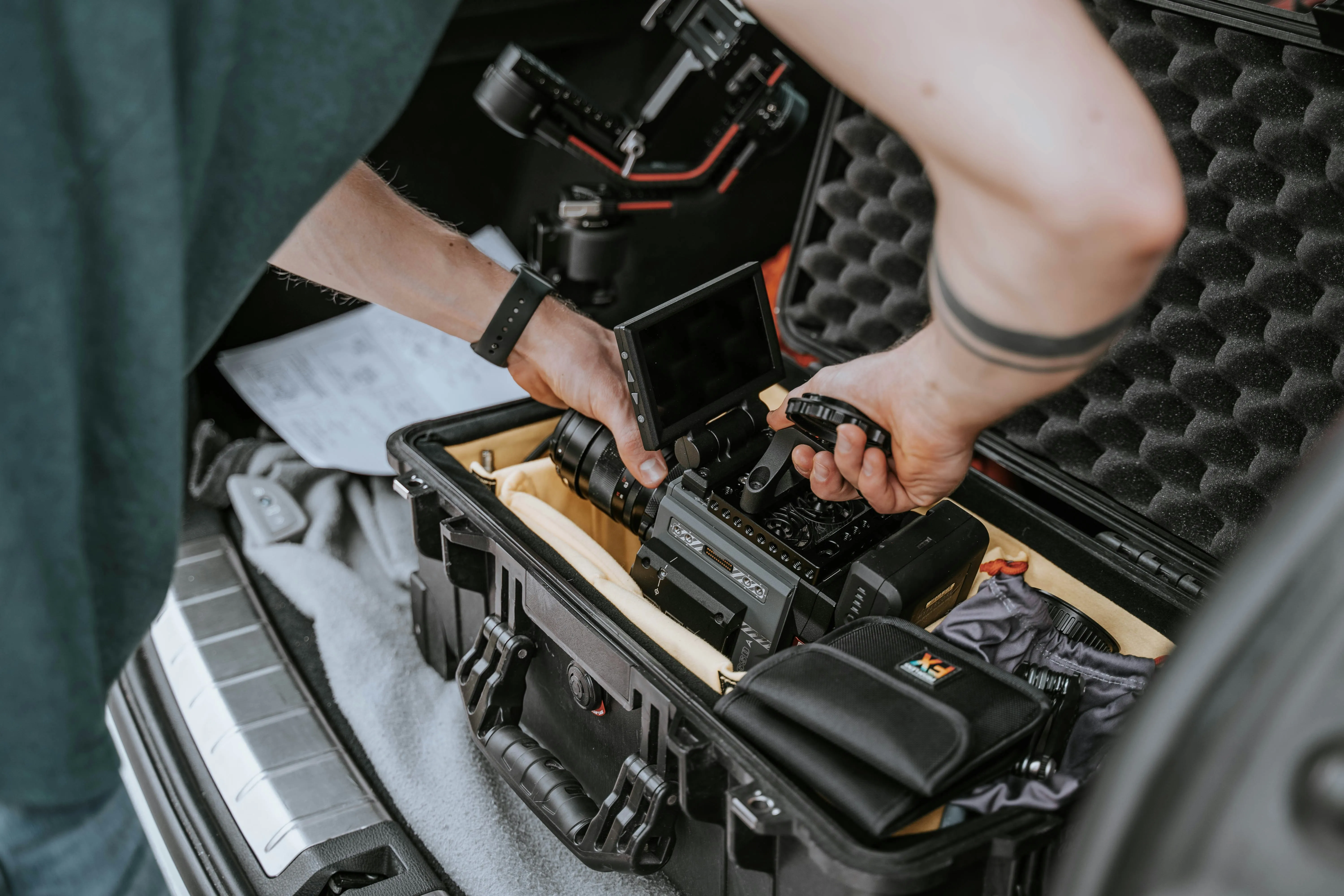 Person rangeant une caméra professionnelle dans une valise de transport rembourrée dans le coffre d'une voiture.