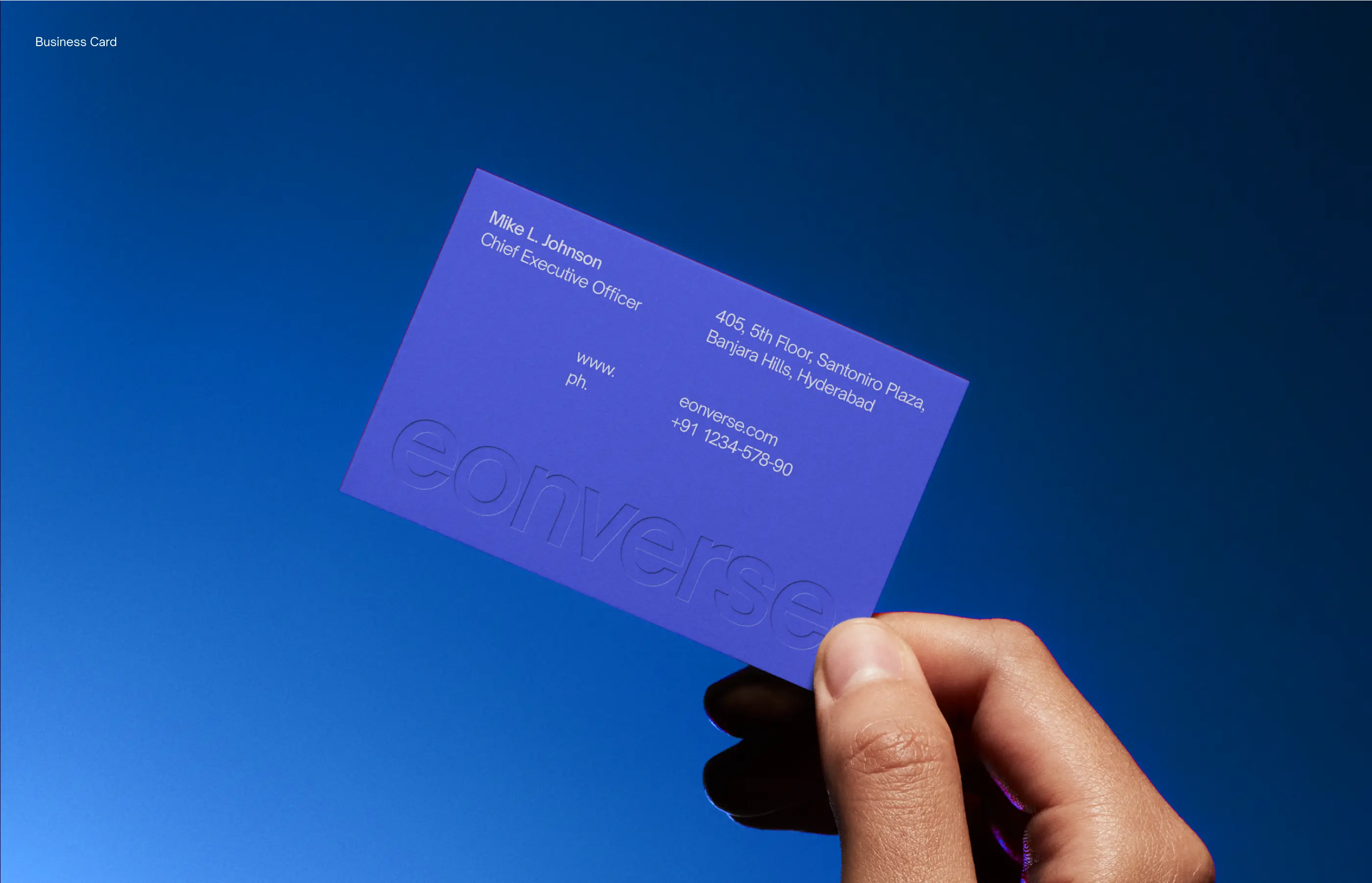 Hand holding blue business card with name Mike L. Johnson, CEO, and Hyderabad address against blue sky.