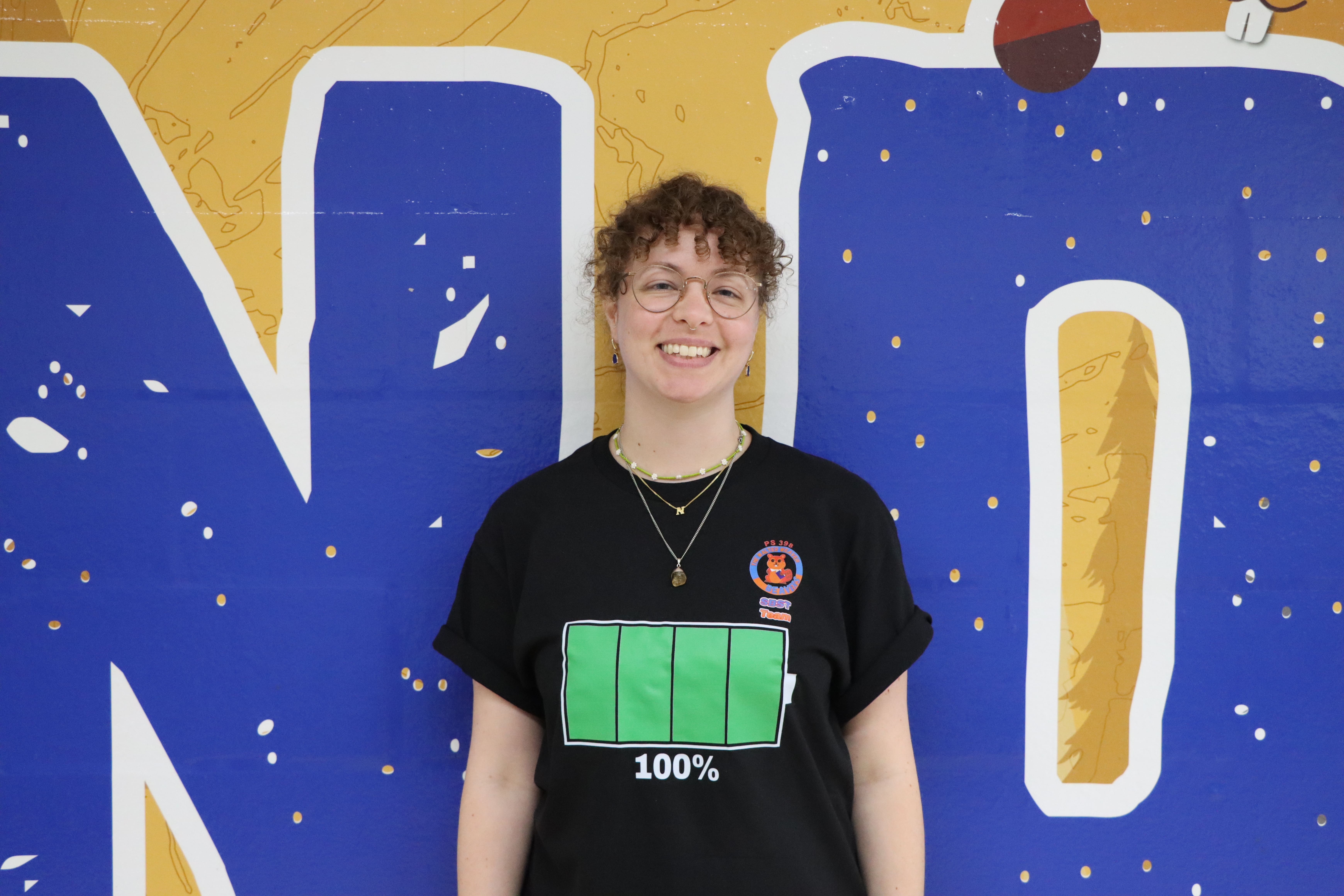 Student wearing battery graphic t-shirt in front of blue mural
