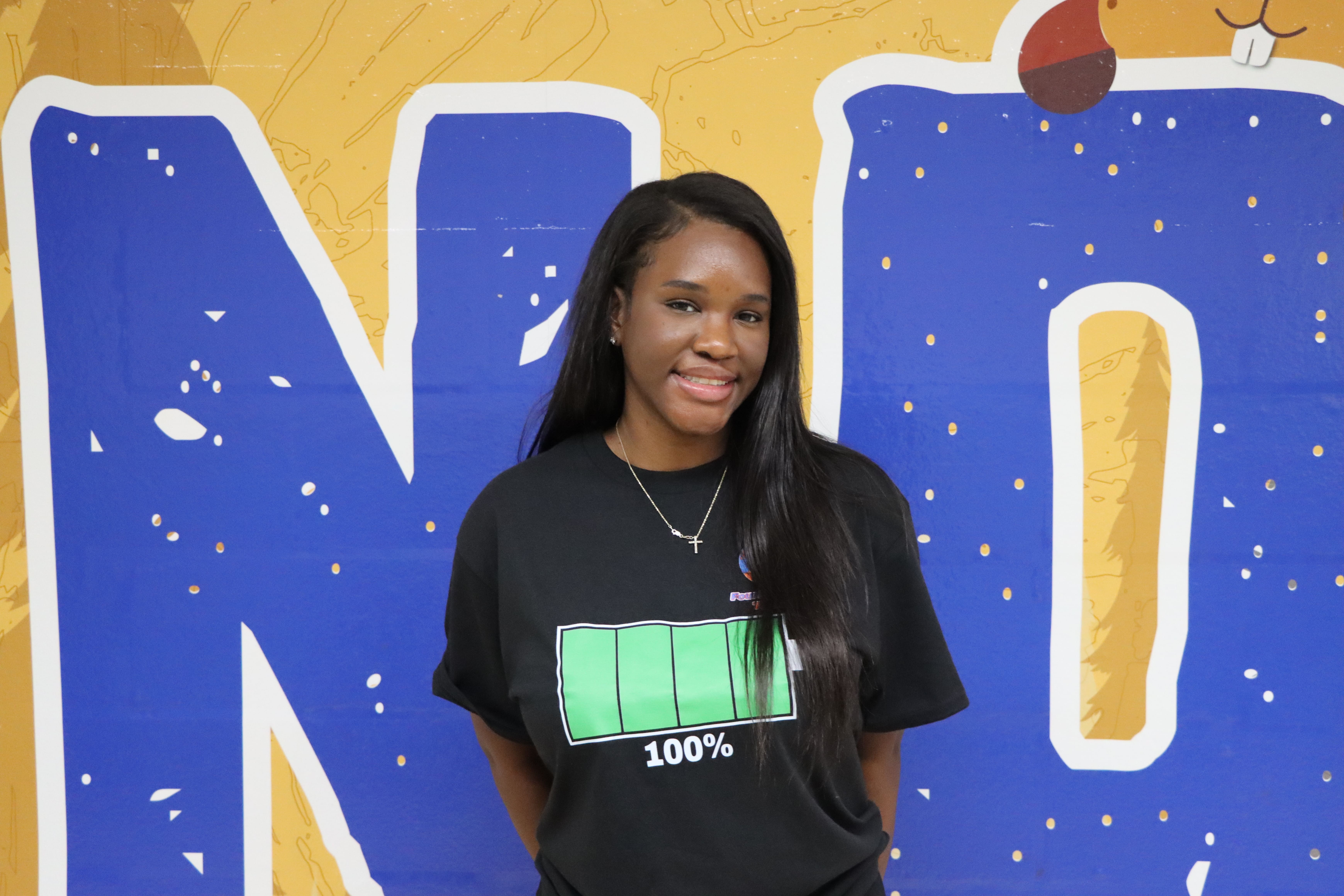 Student smiling in front of blue school mural