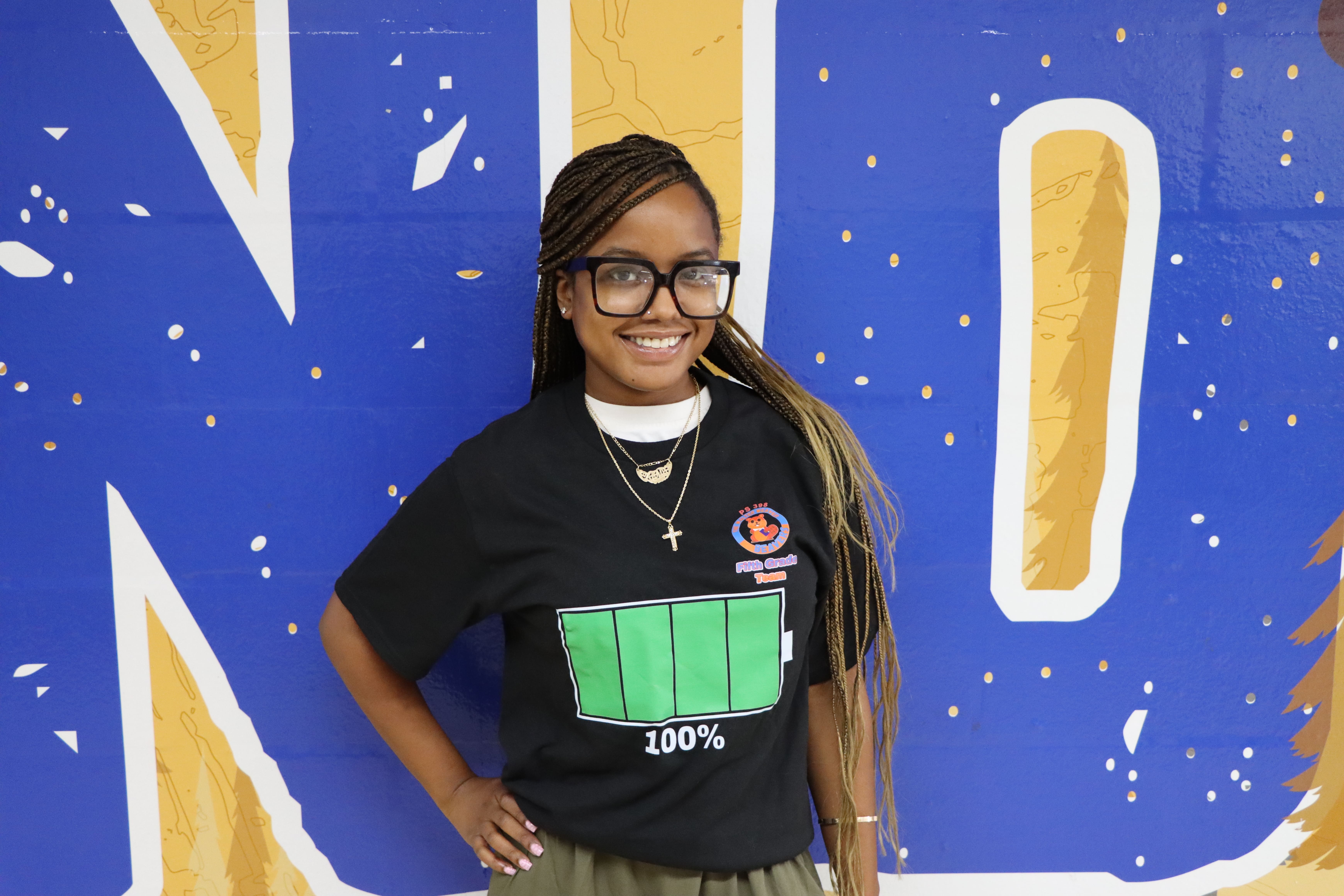 Student smiling in front of blue and gold mural