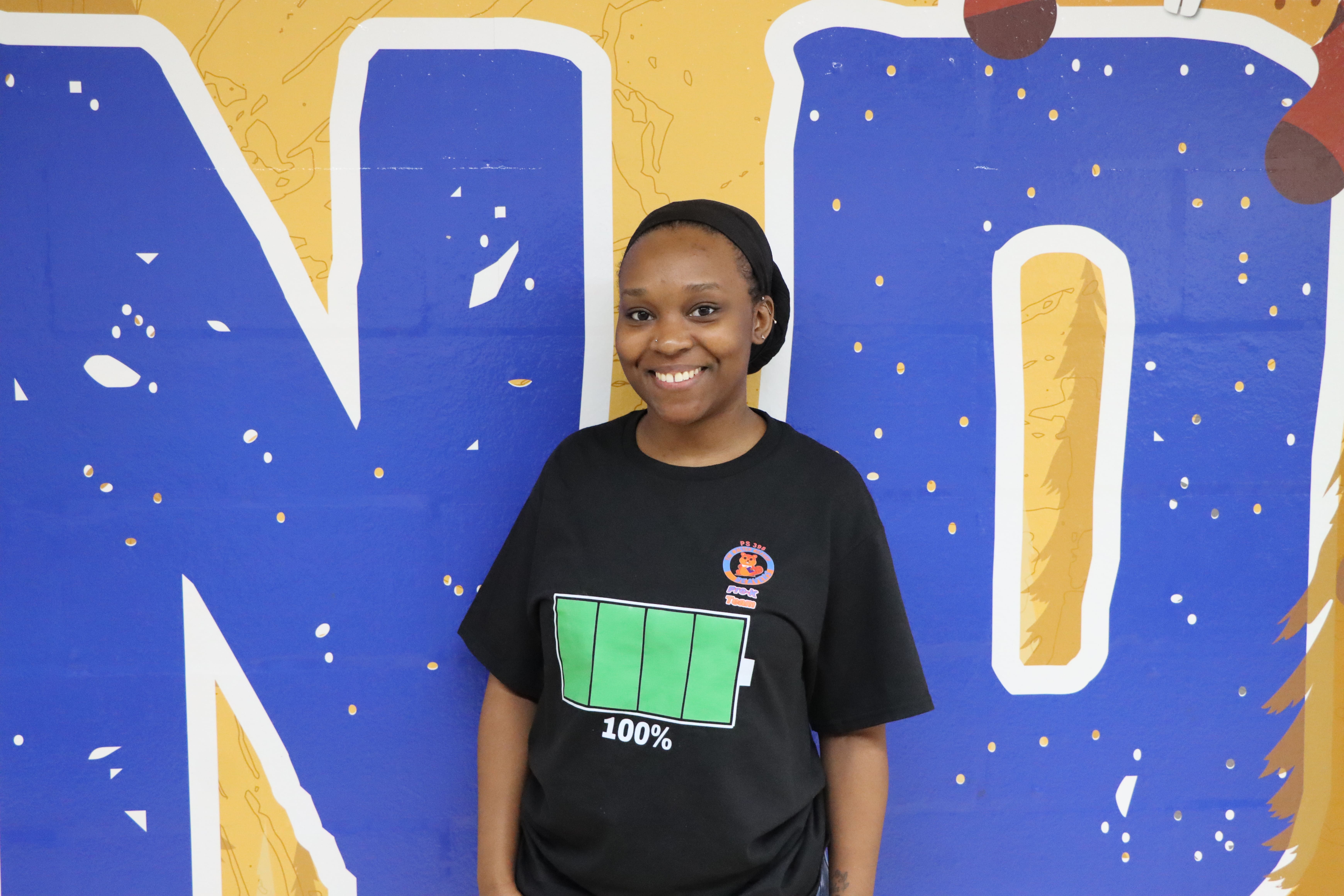 Student smiling in front of blue and yellow mural