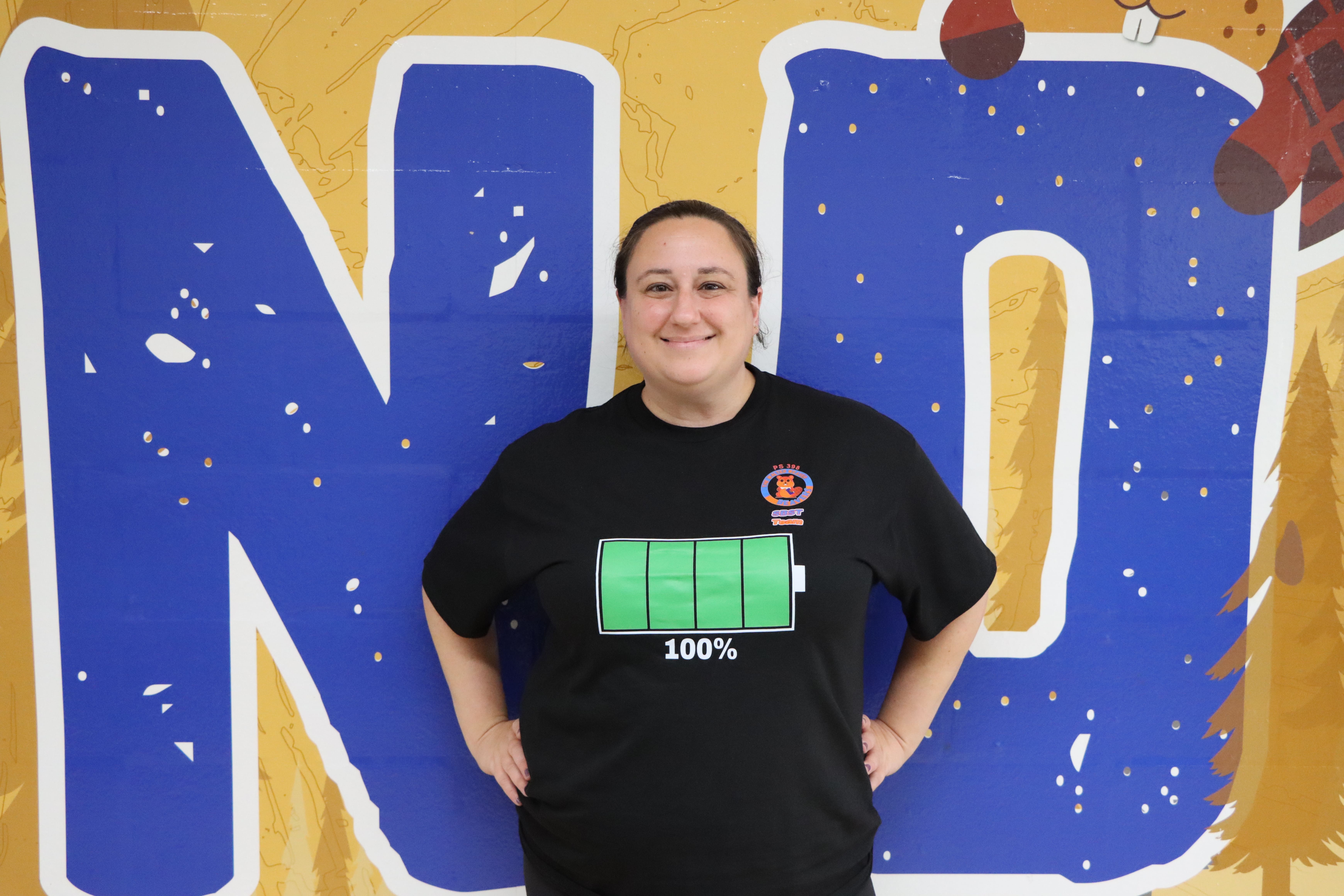 Staff member smiling in front of school mural