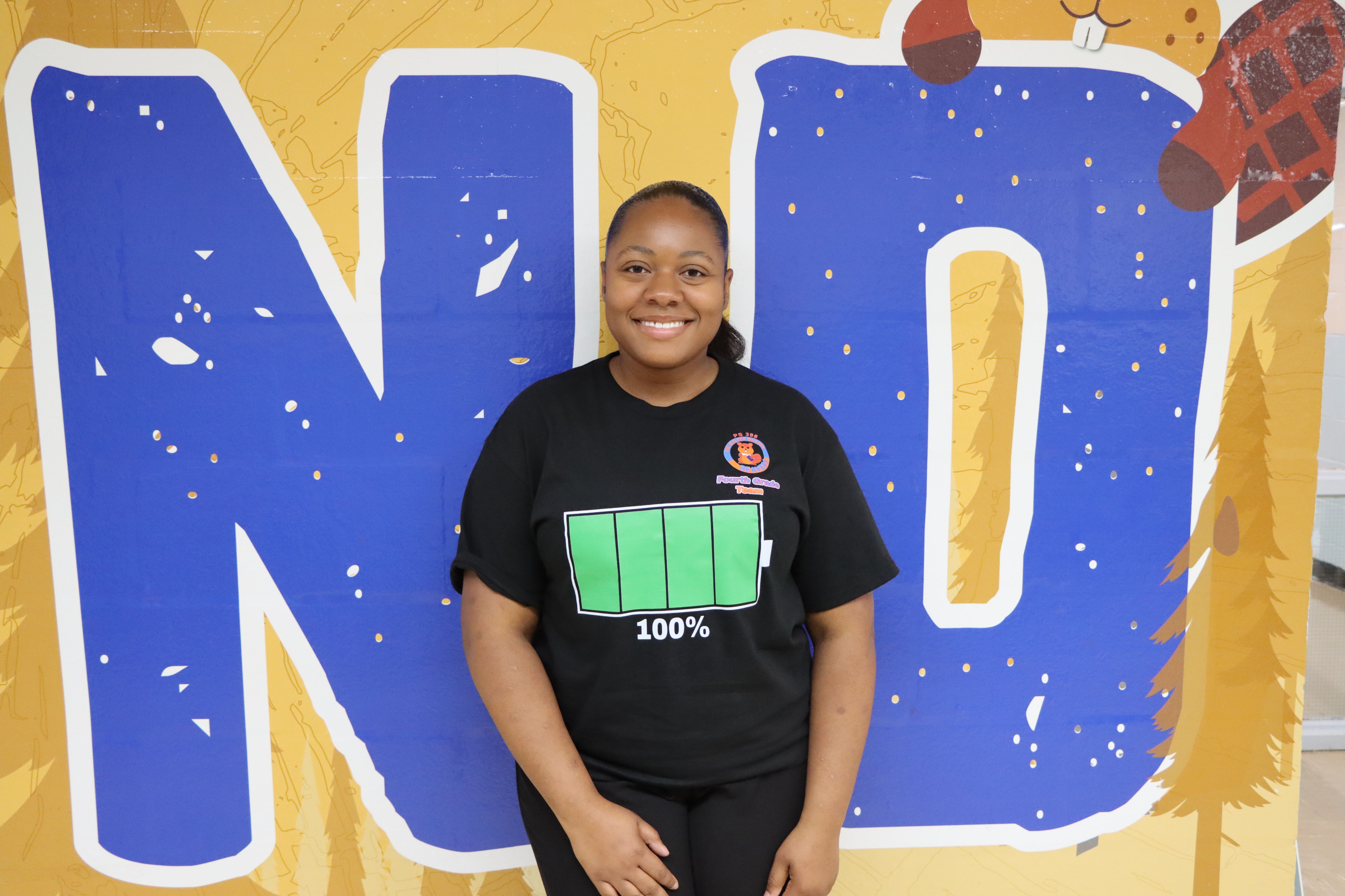 Staff member smiling in front of school mural