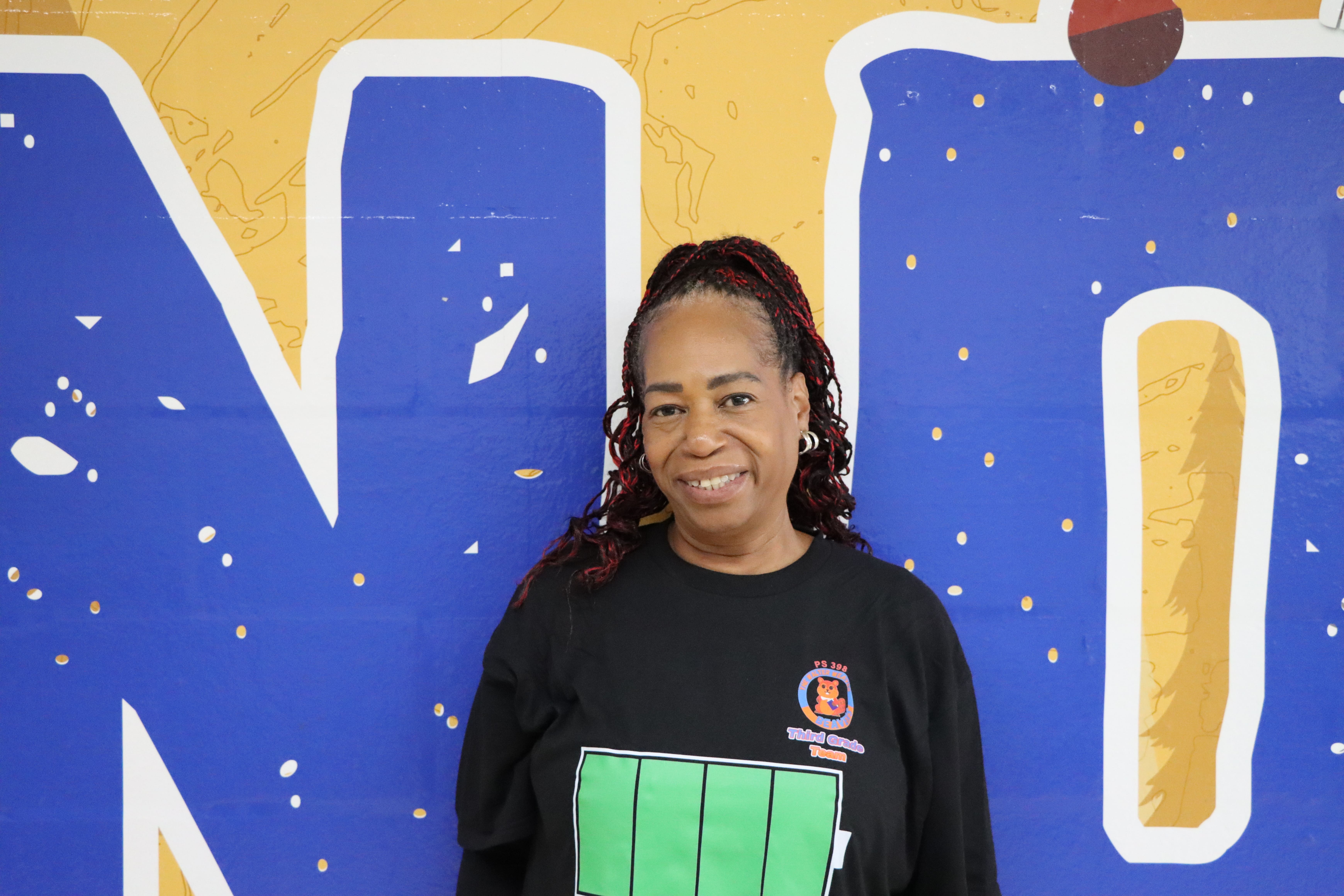 Staff member smiling in front of colorful blue and yellow mural