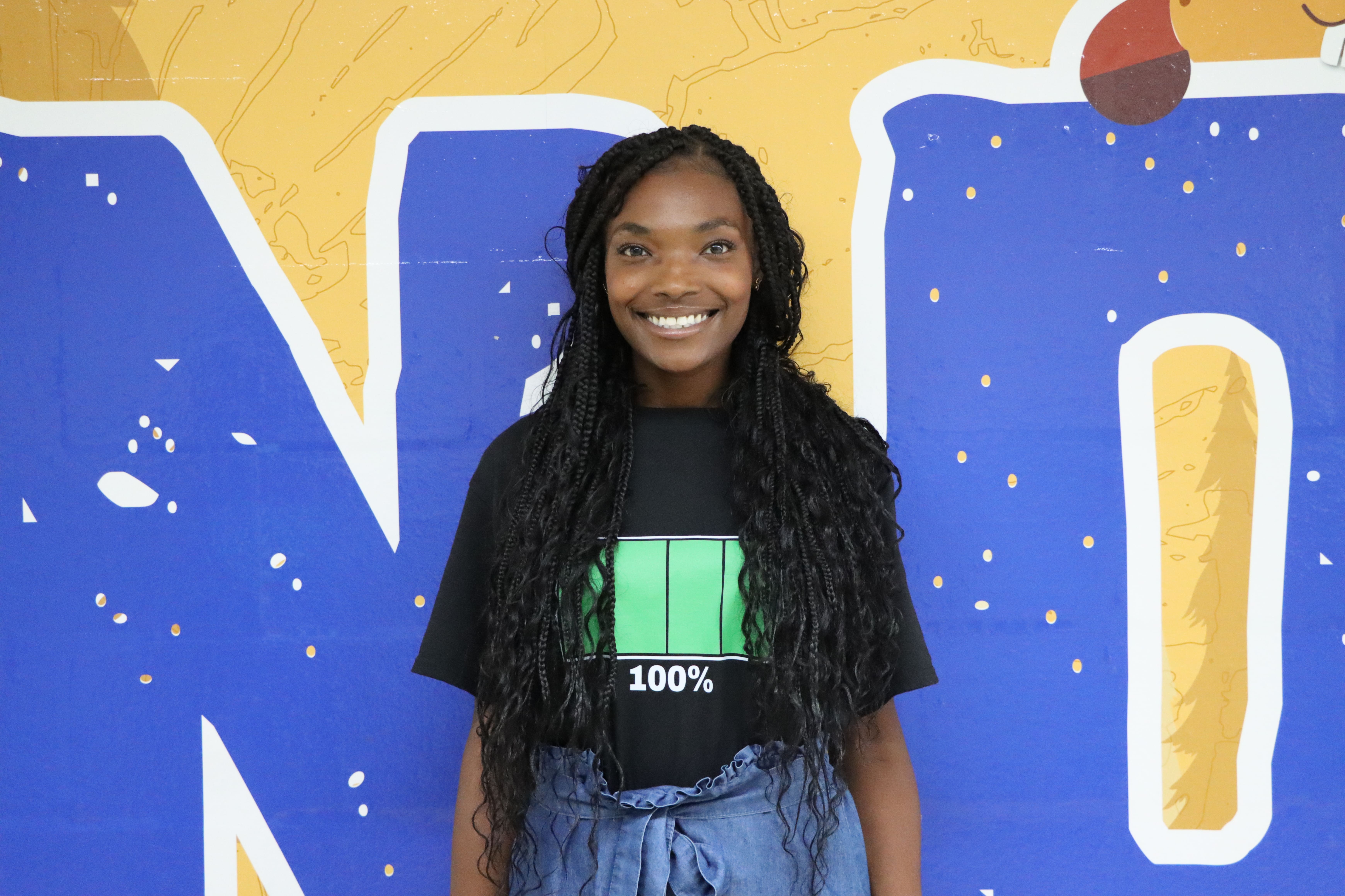 Student smiling in front of colorful blue and yellow wall mural