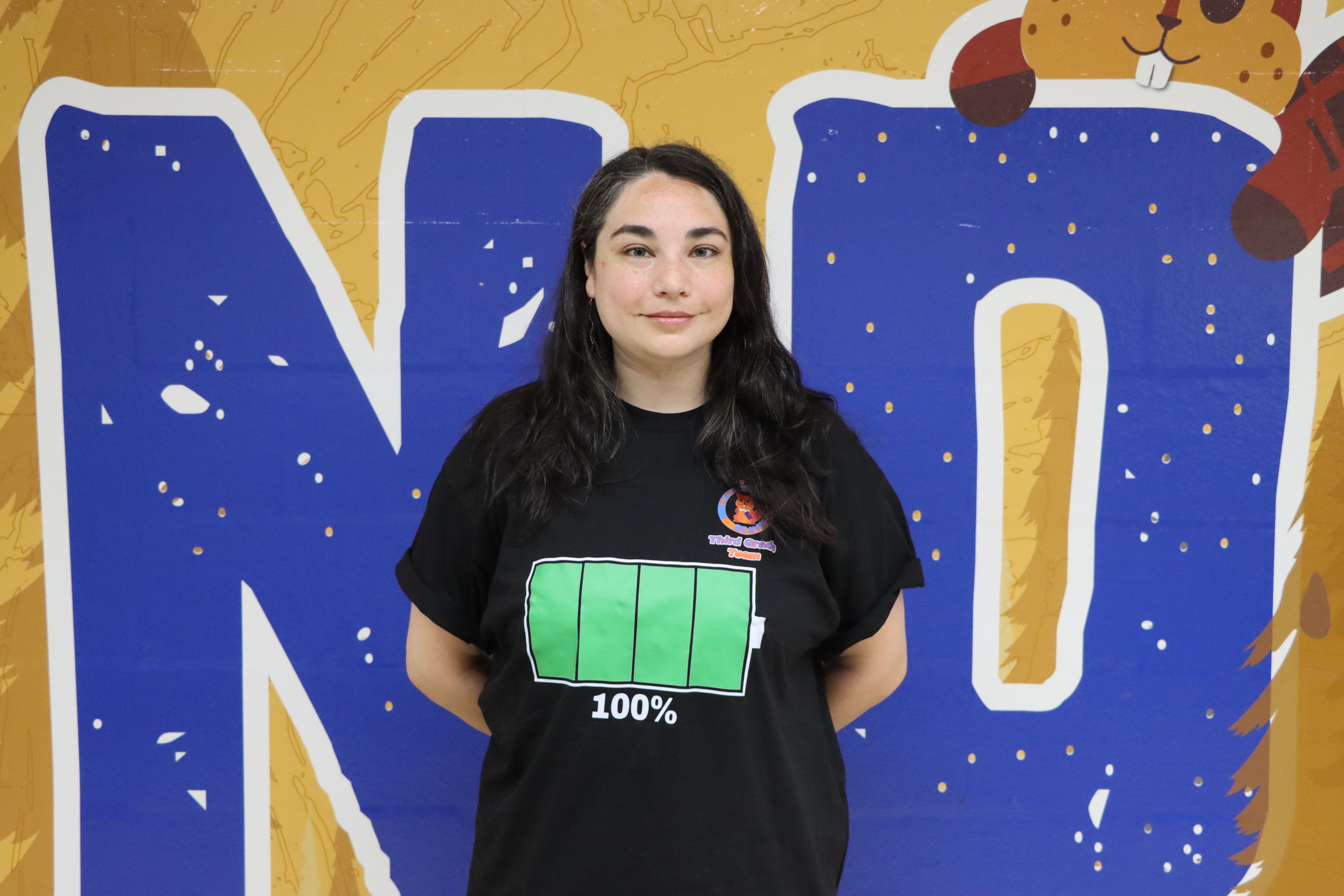 Student wearing battery t-shirt standing against school mural