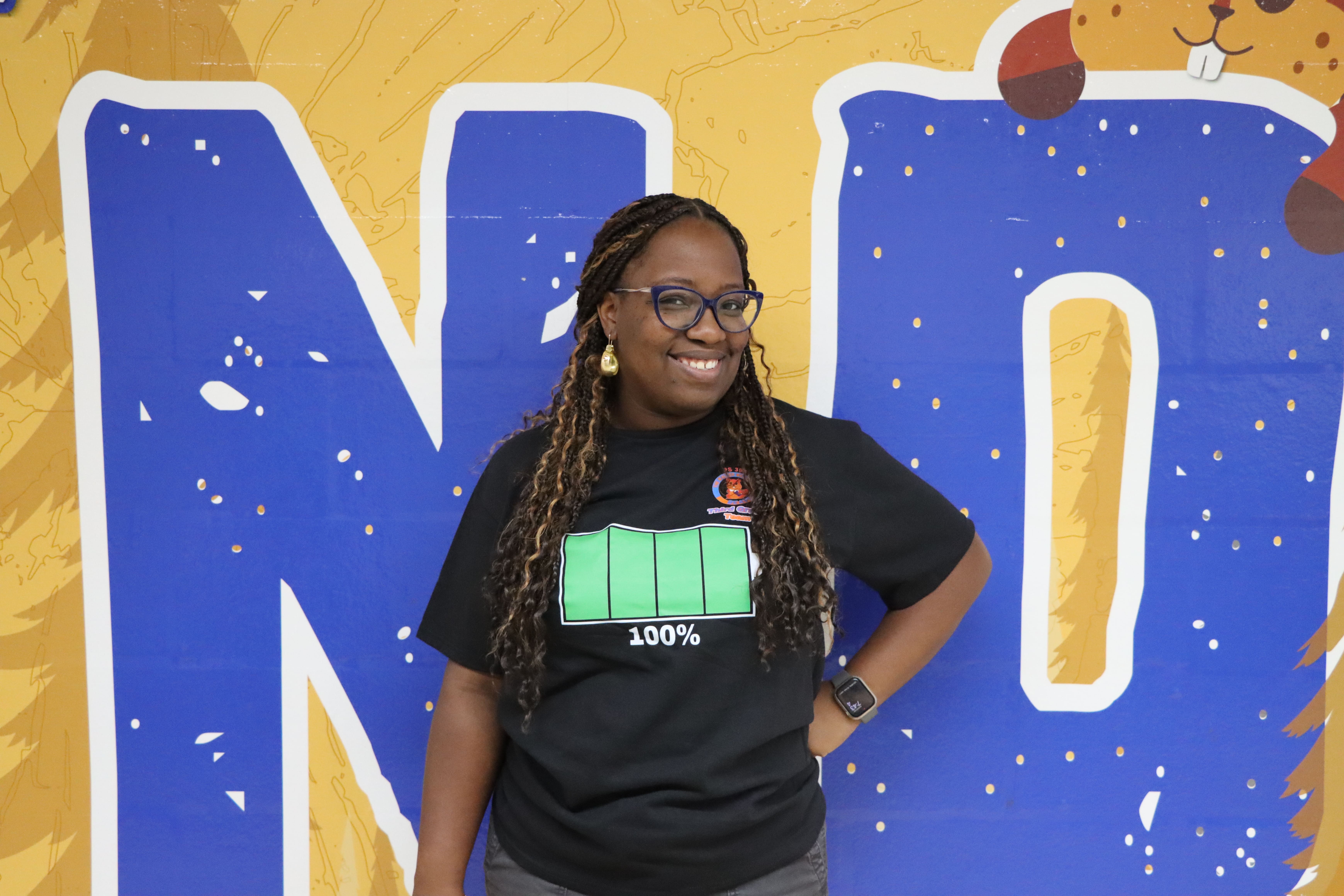 Staff member smiling in front of colorful school mural