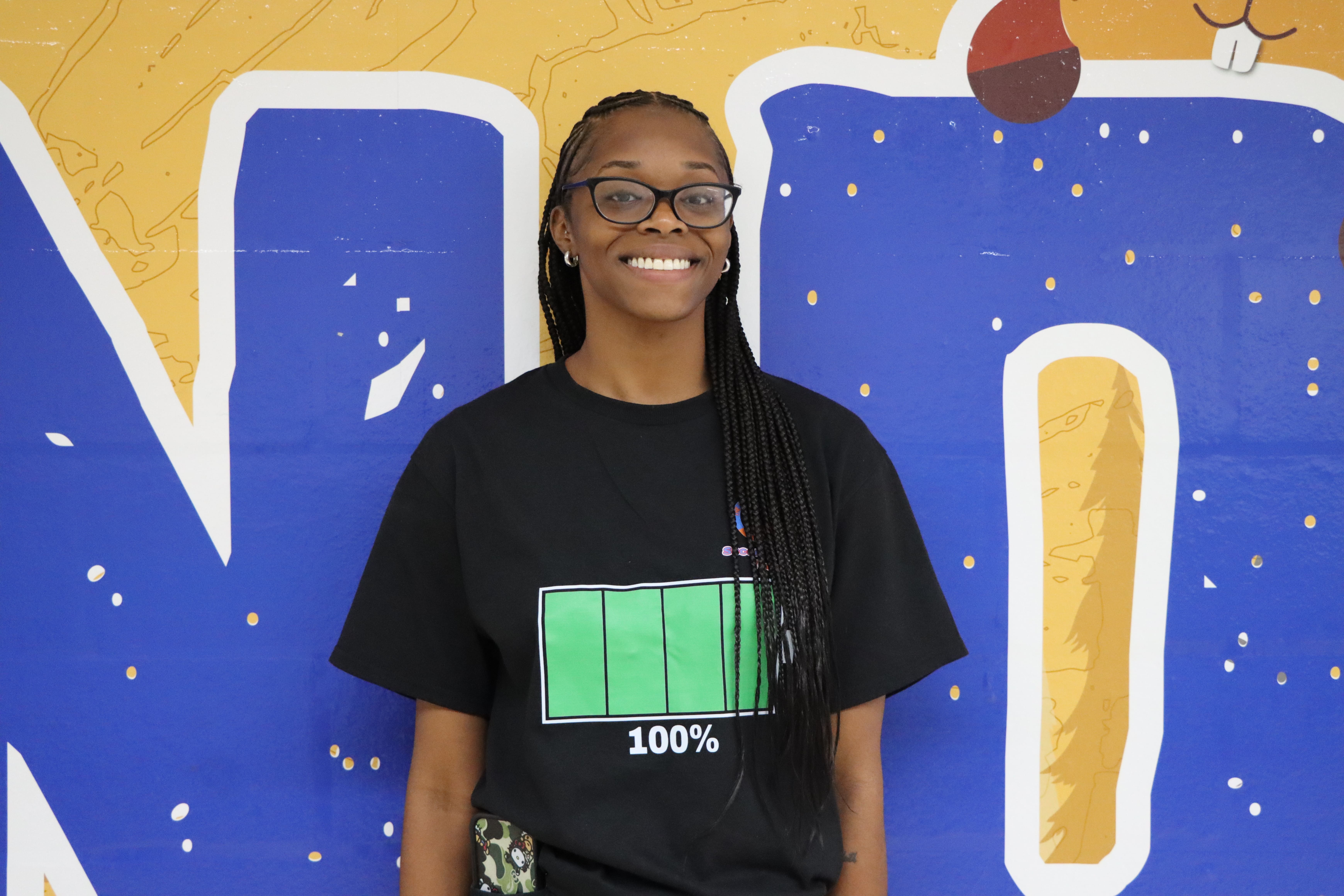 Student wearing battery icon shirt in front of colorful mural