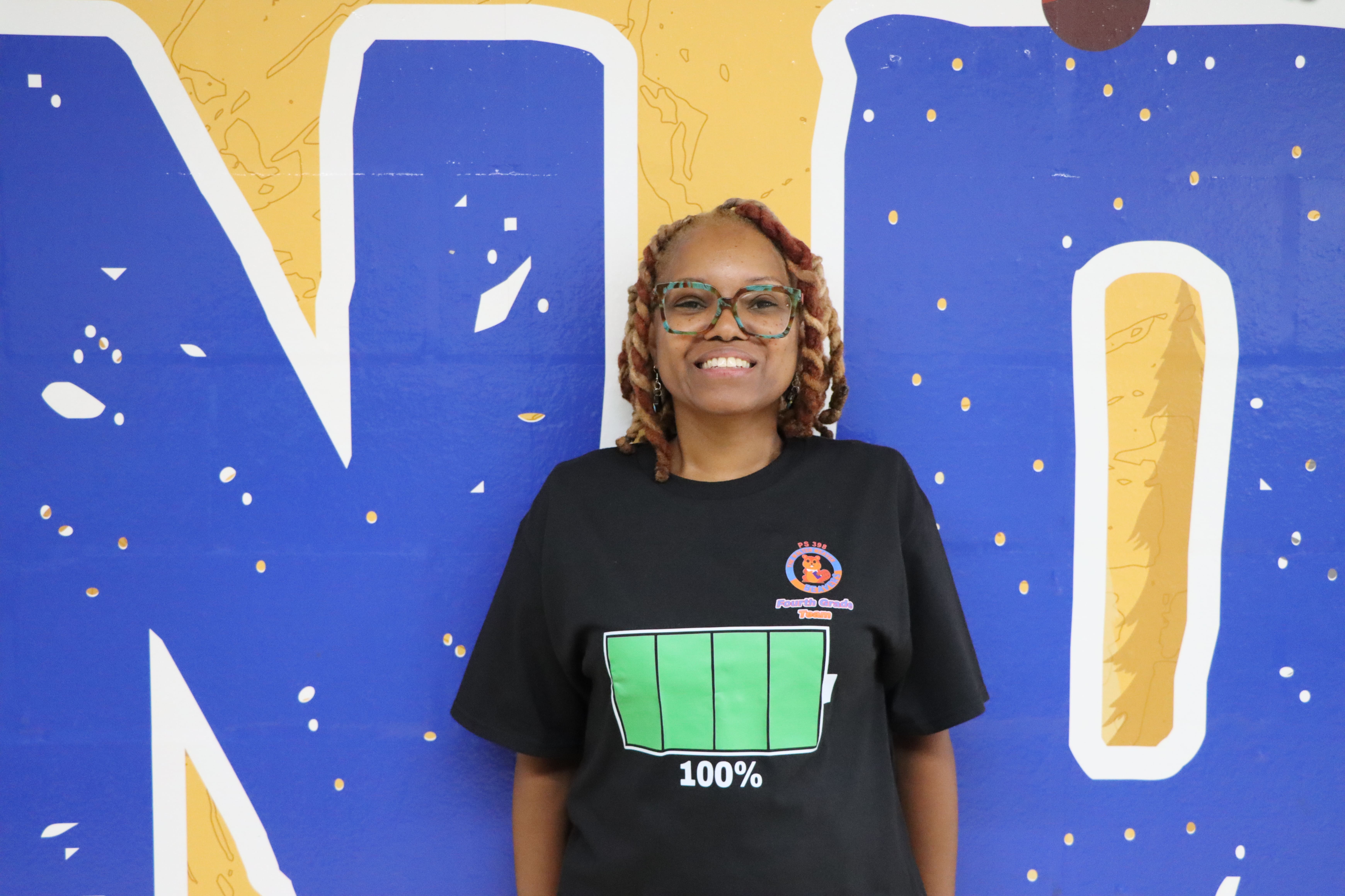 Student smiling in front of blue and yellow mural
