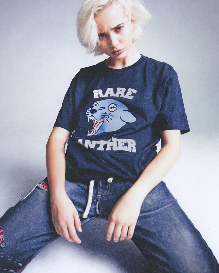Person with short blonde hair wearing a dark shirt with a cartoon panther and text 'RARE PANTHER'.
