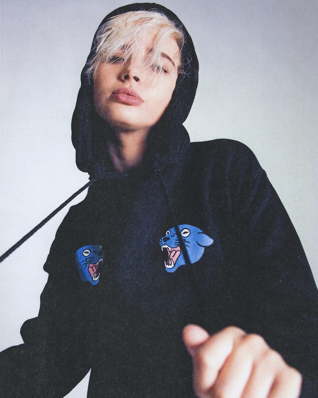 Person with light blond hair wearing a black hoodie with blue roaring panther faces on chest.