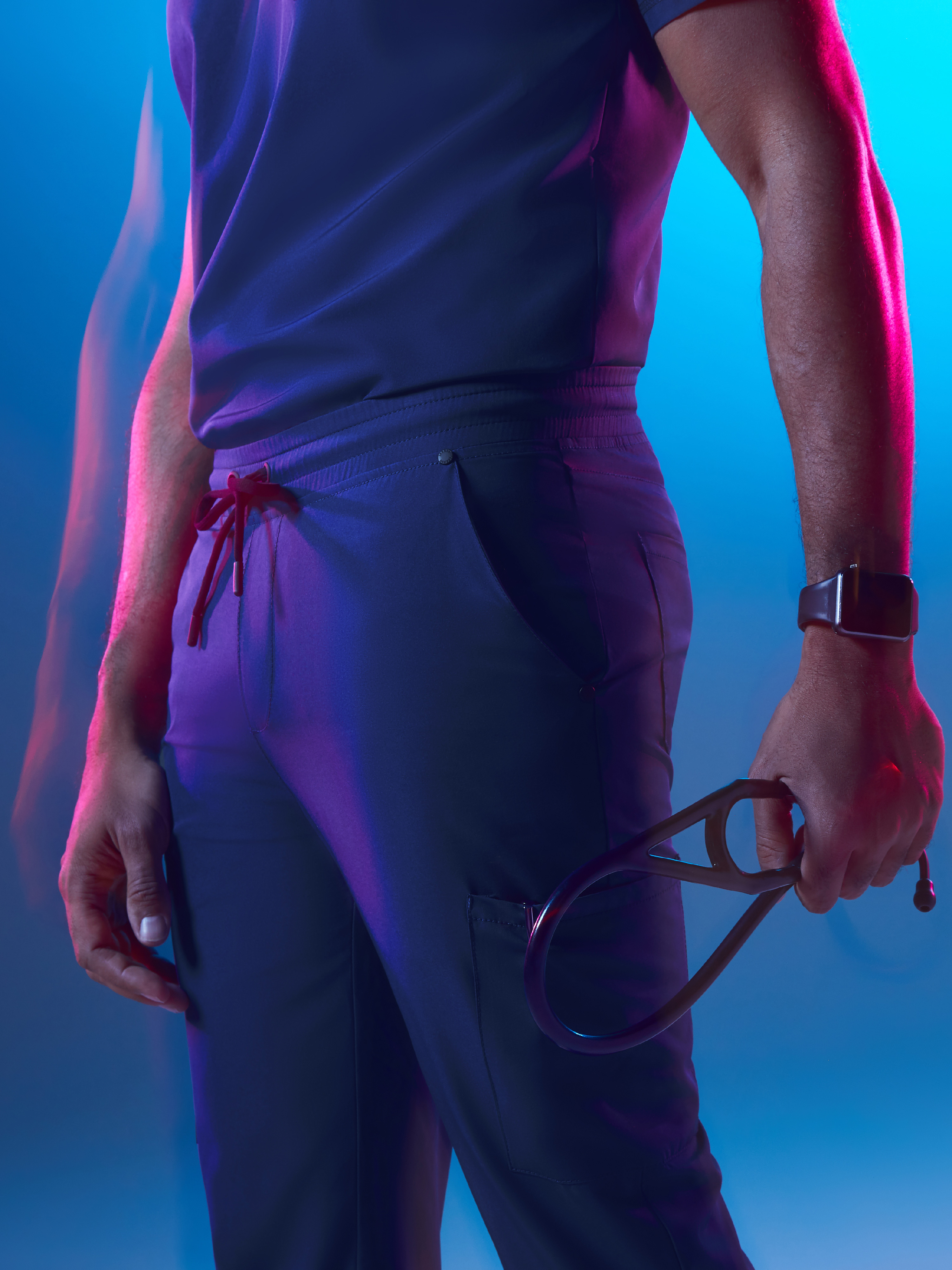 Man in blue scrubs balancing on one hand on a white block against blue light background.