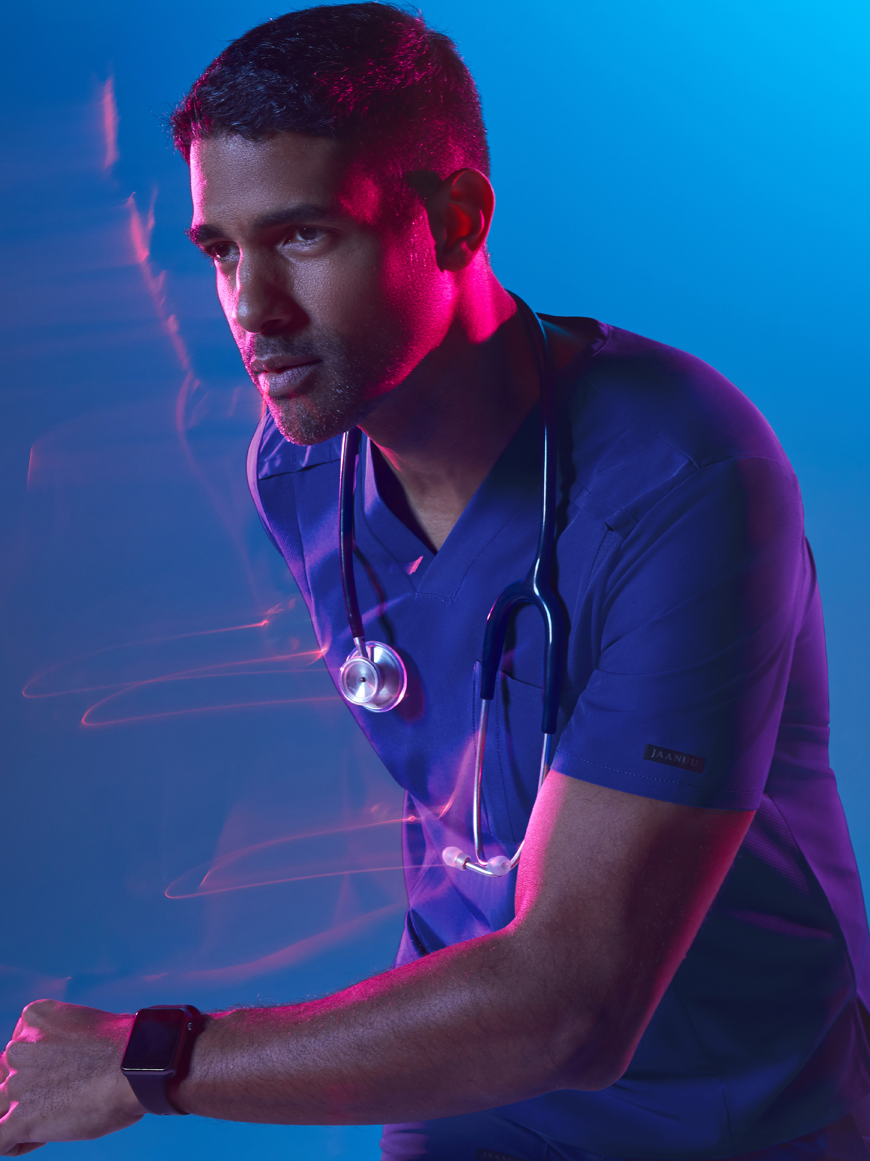 Man in blue scrubs balancing on one hand on a white block against blue light background.