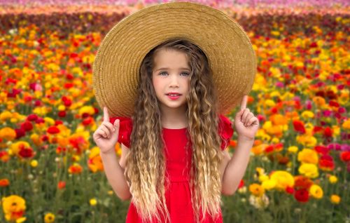 A Professional iPhone Photography image of a young girl in a red dress playing in a field of red and yellow flowers
