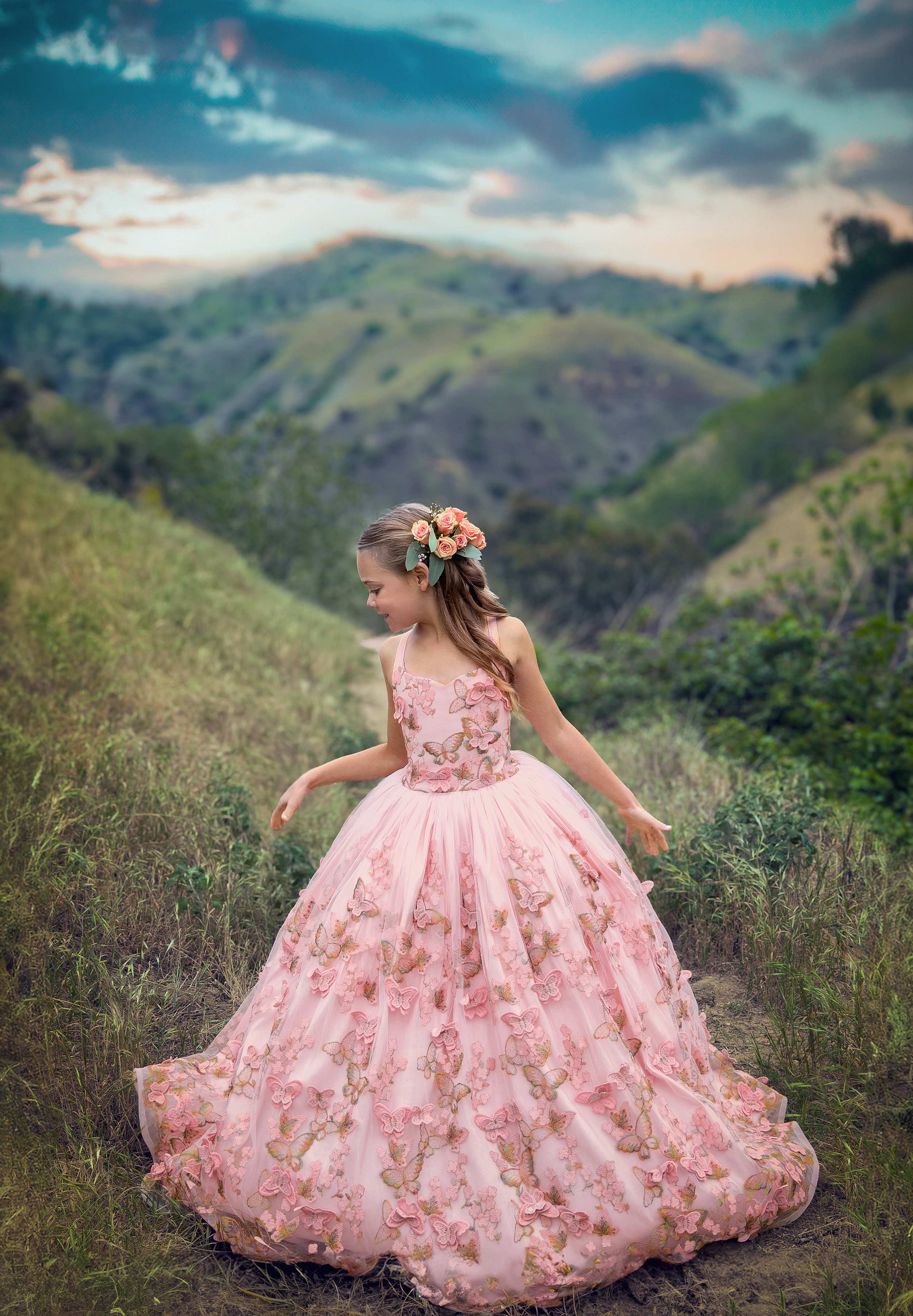 A toddler girl in a long pink princess dress explores a mountain trail