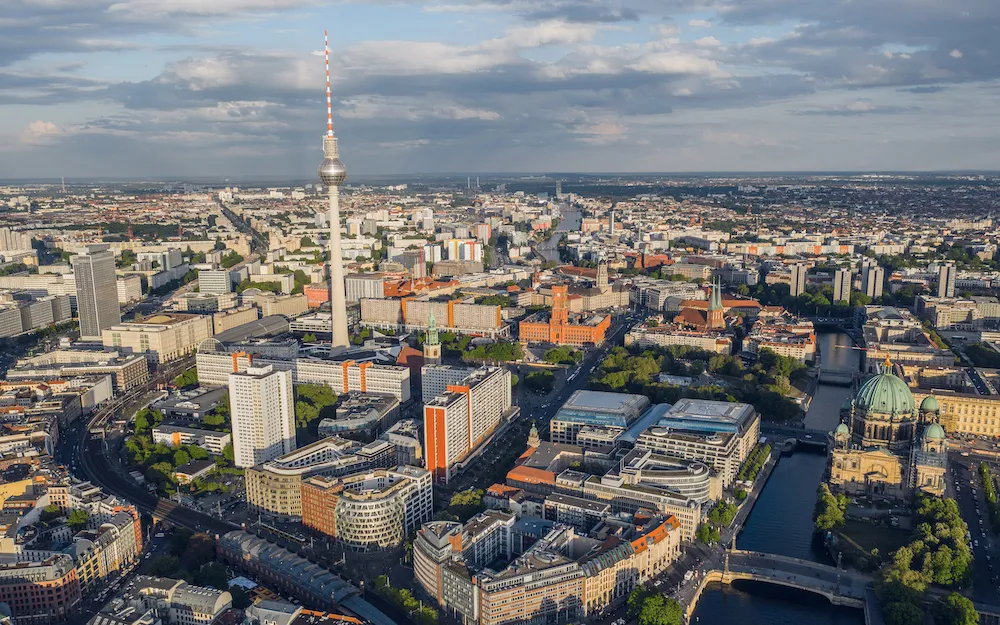 Luftaufnahme von Berlin bei sonnigem Wetter mit dem markanten Fernsehturm, der Spree und historischen Gebäuden.