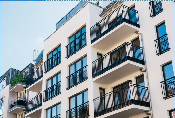 Fassade eines modernen Wohngebäudes mit weißen Wänden und schwarzen Balkongeländern unter blauem Himmel.