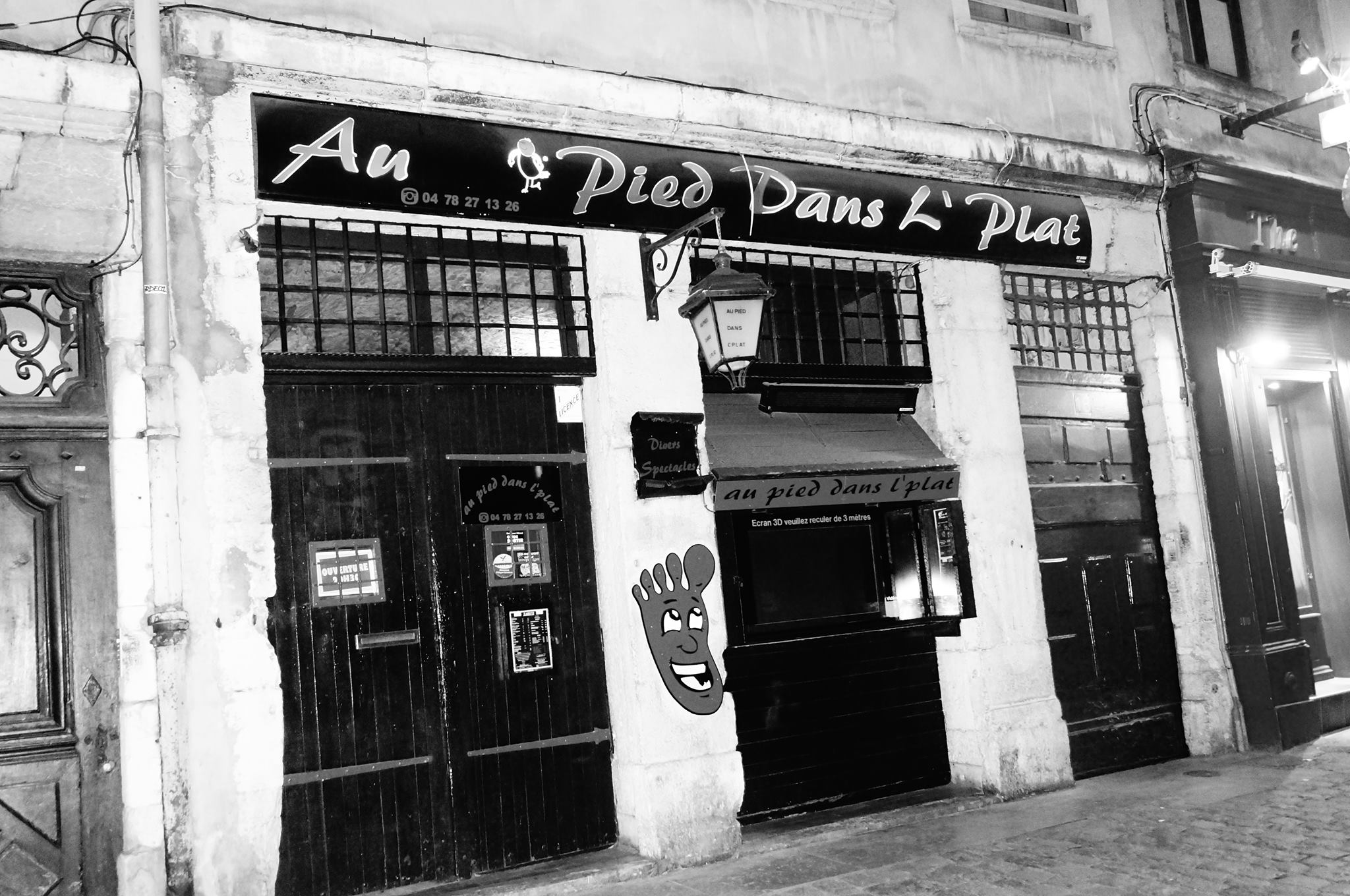 Photo en noir et blanc du cabaret au pied dans l'plat. Devanture assez ancienne avec un pied 