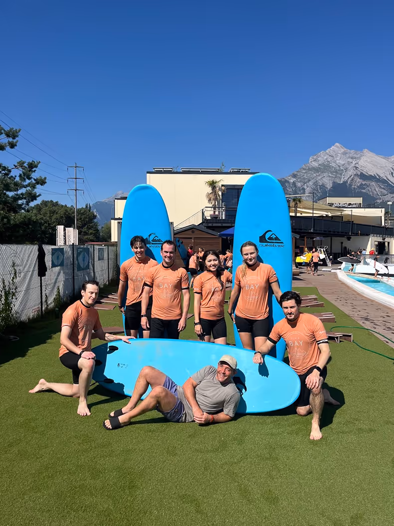 Group of people in orange shirts posing outdoors with blue surfboards