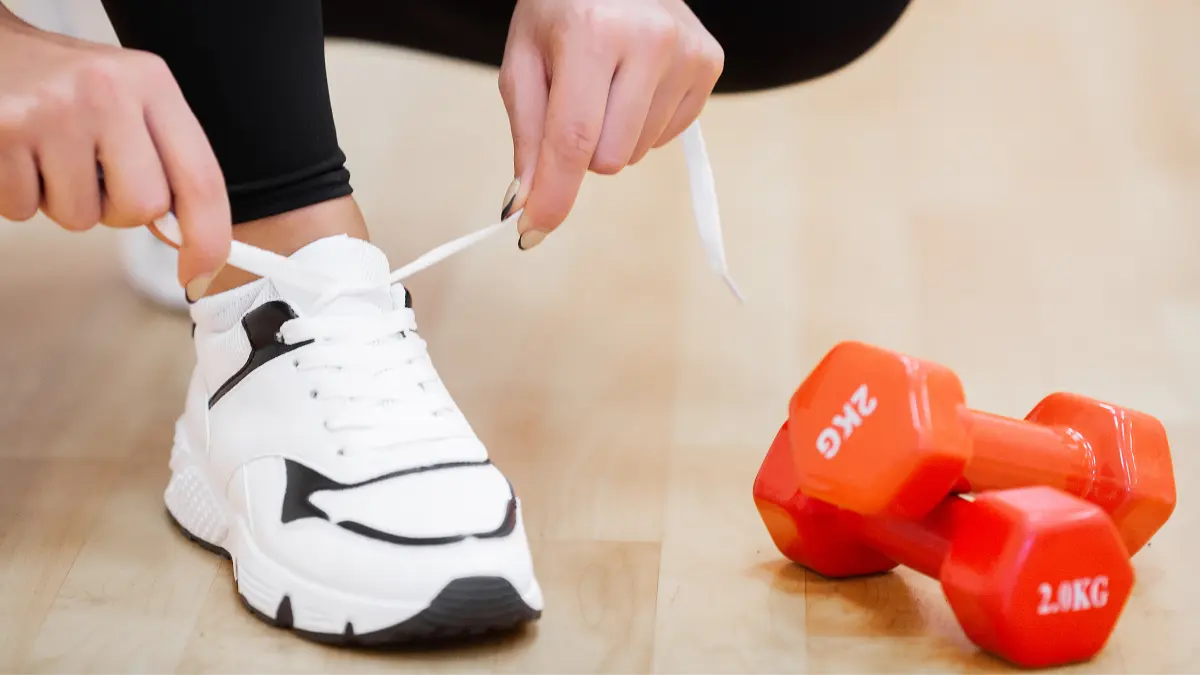 Žena vee sportske tenisice spremajući se za fizičku aktivnost