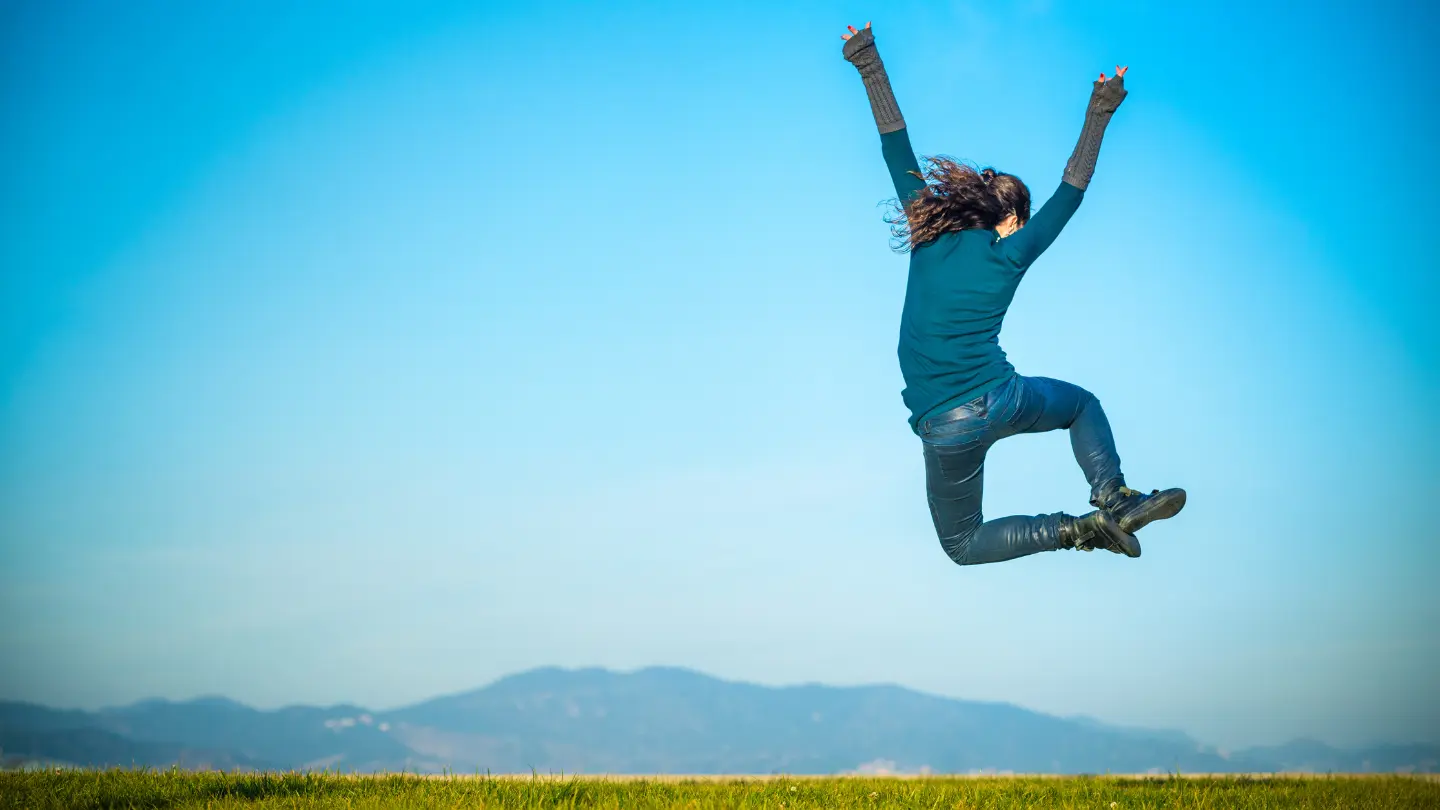 sretna djevojka skače na livadi što signalizira sreću i zdravlje