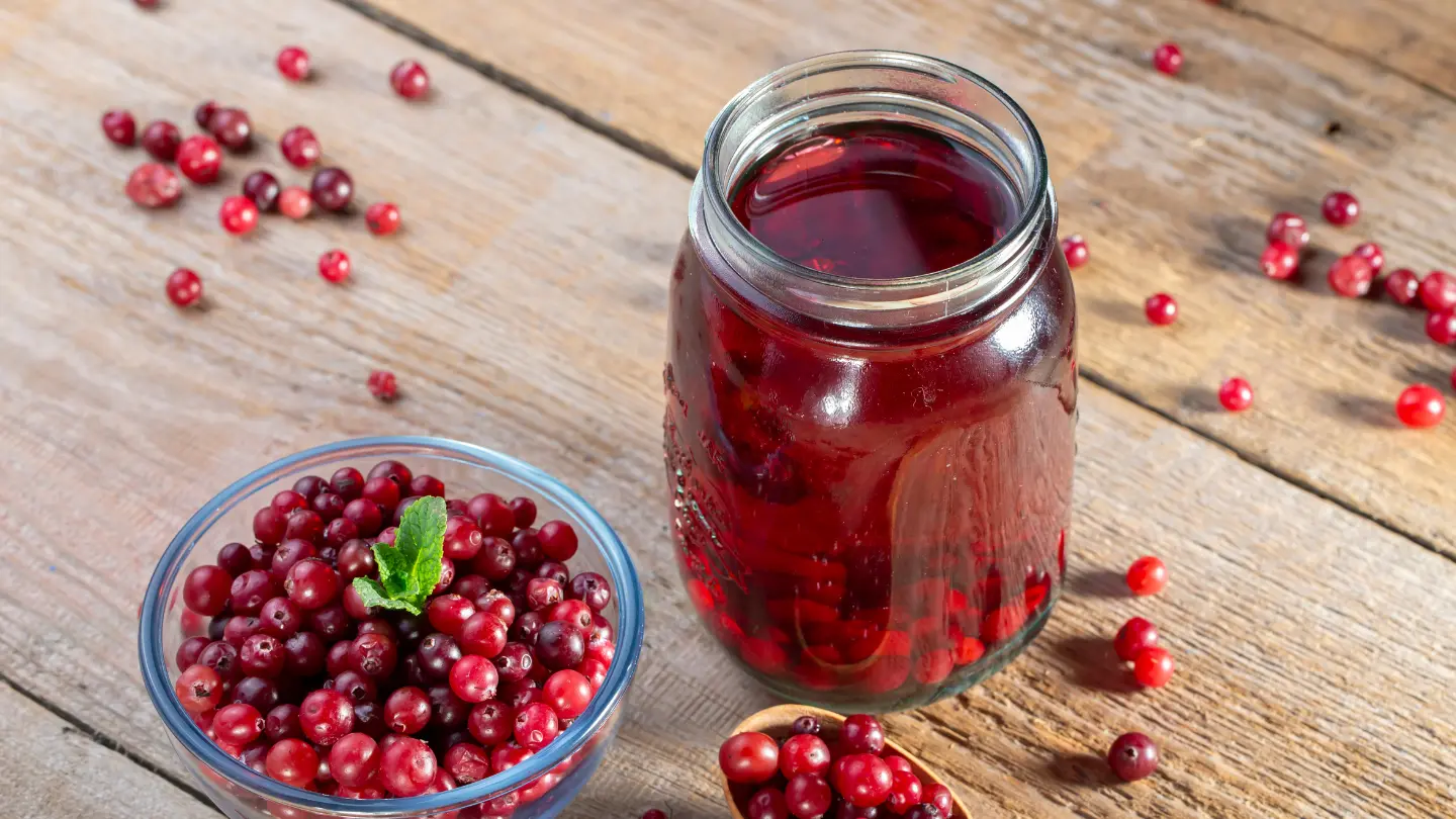 svježi sok od brusnica u tegli pokraj svježih brusnica na stolu