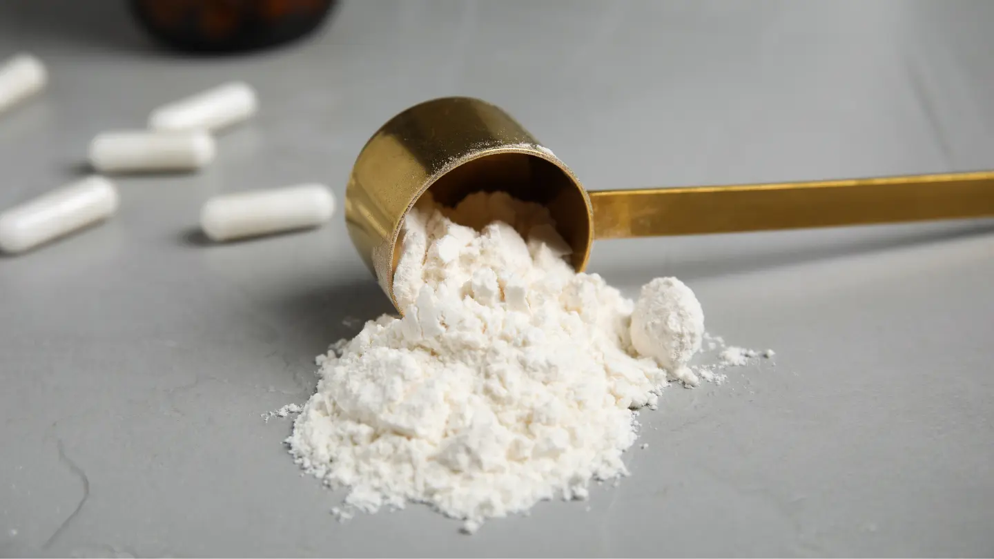 zlatna mjerica s kreatin monohidrat prahom posutim po stolu