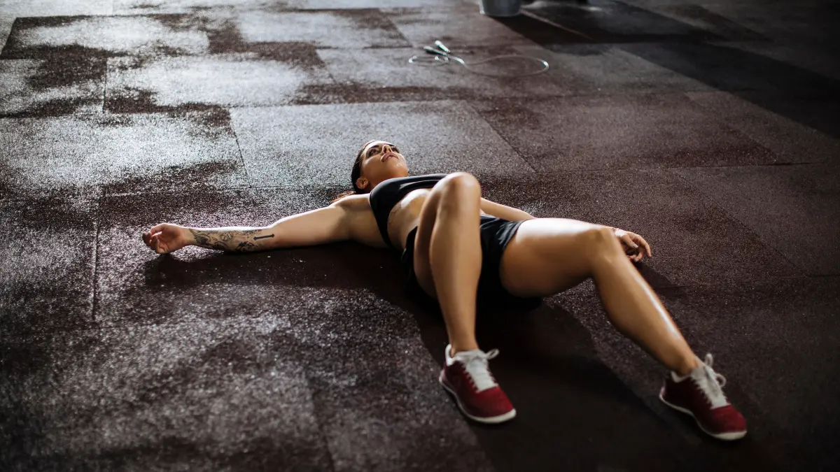 Žena umorna nakon treninga u postu leži na podu teretane