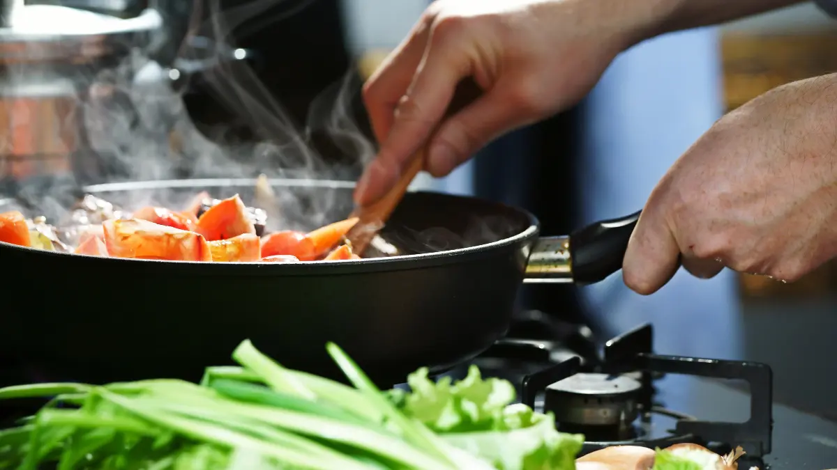a man cooking food on a pan, mixing it with a wooden spoon