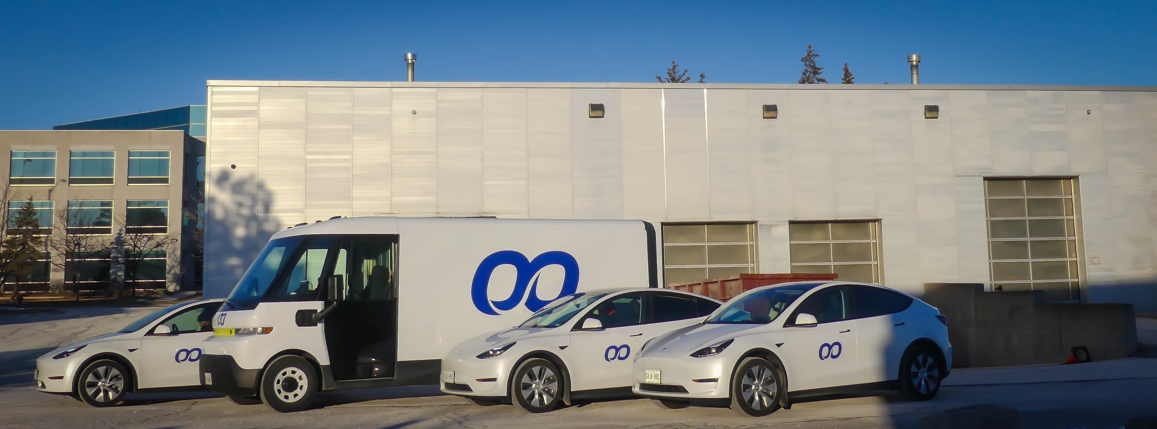 White Koorier delivery fleet featuring an electric van and cars with koorier's purple logo parked in front of a logistics facility.