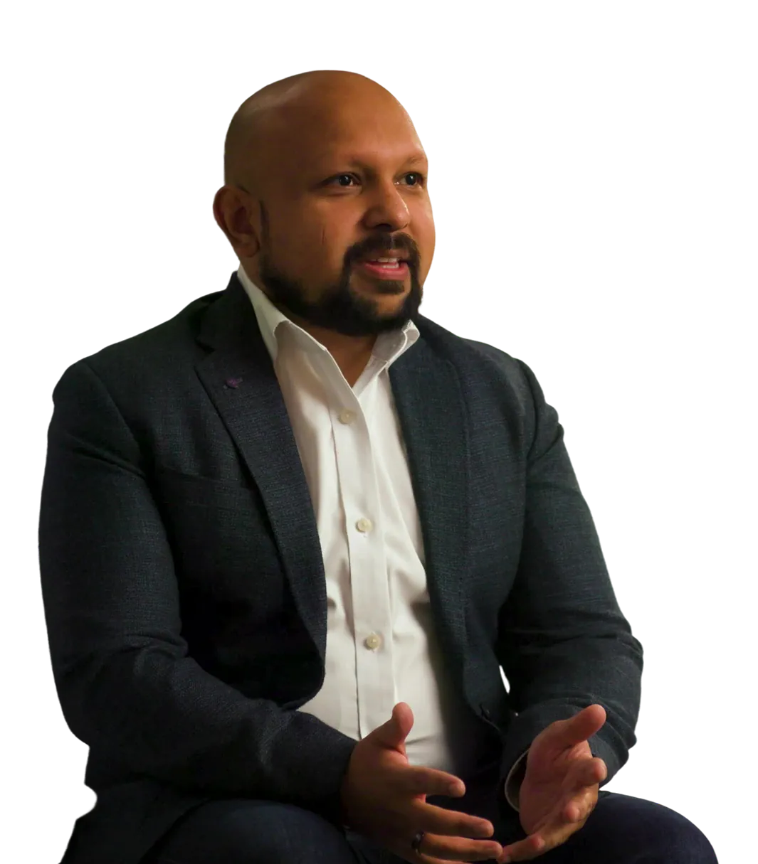 Bald man with a beard wearing a dark suit jacket and white shirt, speaking with hands gesturing.
