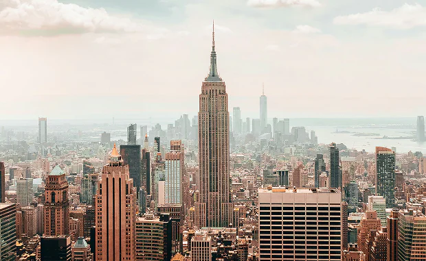 Panoramic view of New York City skyline with the Empire State Building prominently in the center under a cloudy sky.