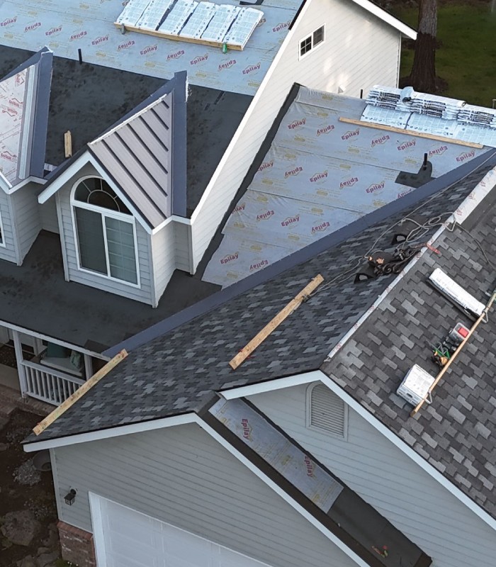 Aerial view of a house roof in mid-construction with shingles and roofing materials visible.
