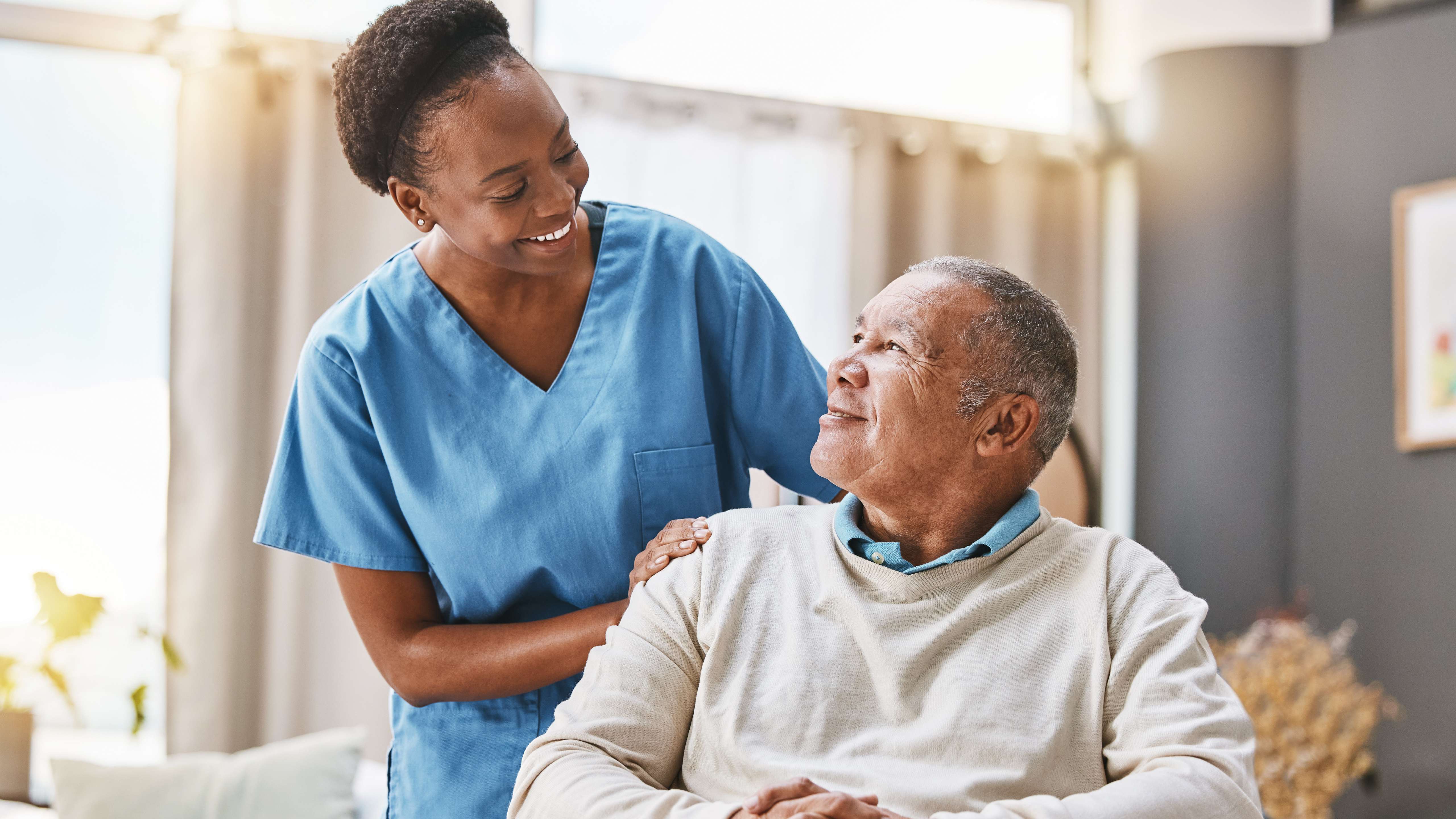 A healthcare worker in blue scrubs works with a man in a SNF