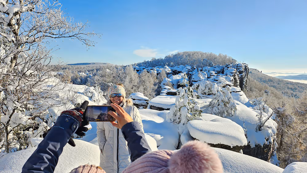Guest being photographed at snowy cliff viewpoint overlooking the sandstone rock towers of Tisa Rocks in Bohemian Switzerland.