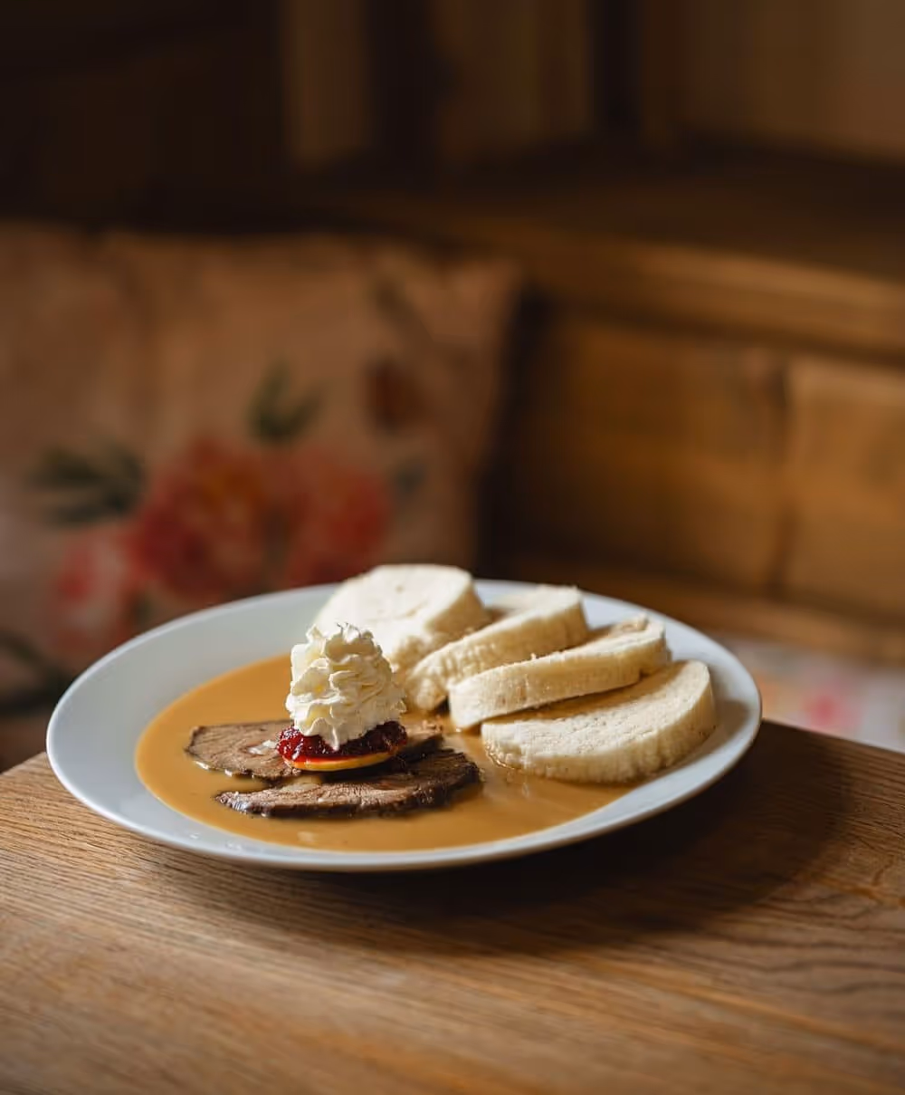 Traditional Czech dish with dumplings and creamy sauce served in a rustic restaurant setting.