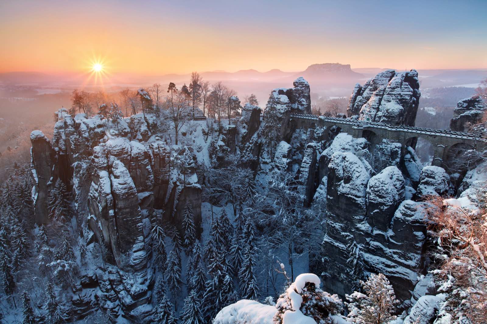 Bastei Bridge and snow-covered sandstone rocks at sunrise in Saxon Switzerland.