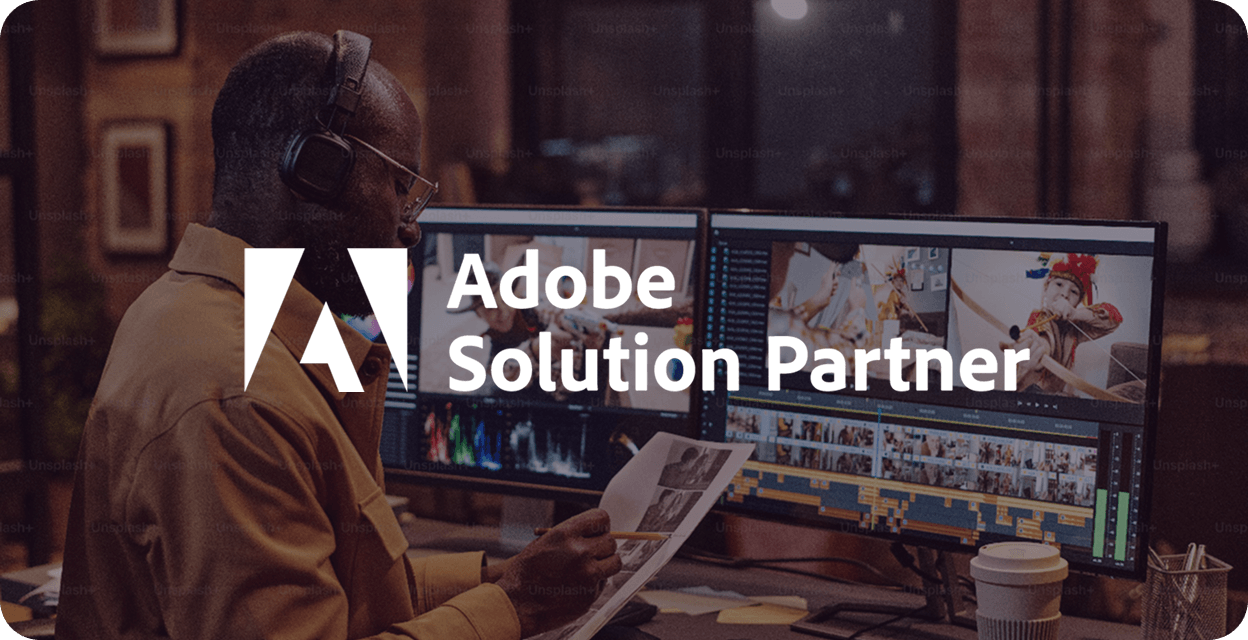 Person wearing headphones working on video editing with dual monitors in a studio, overlaid with Adobe Solution Partner logo.