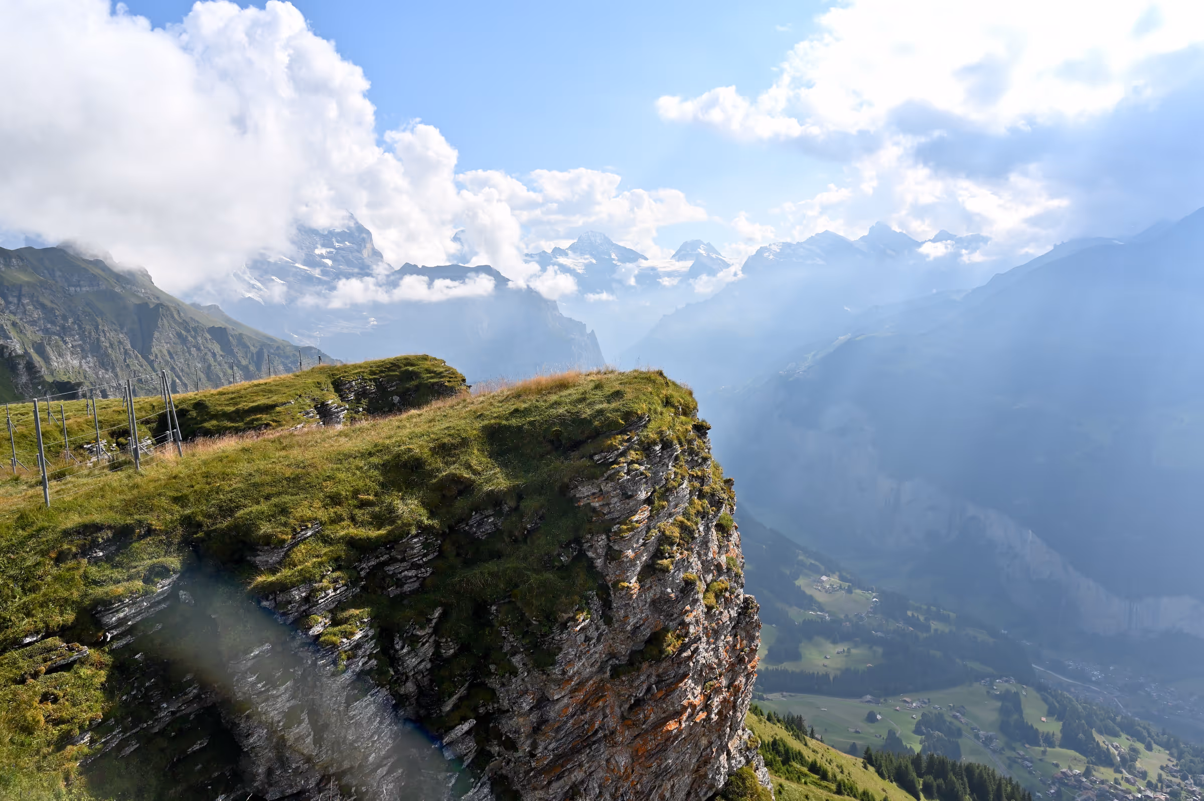 Lift hub at Männlichen with grassy alpine terrain, visitors, and Bernese Alps in the background.