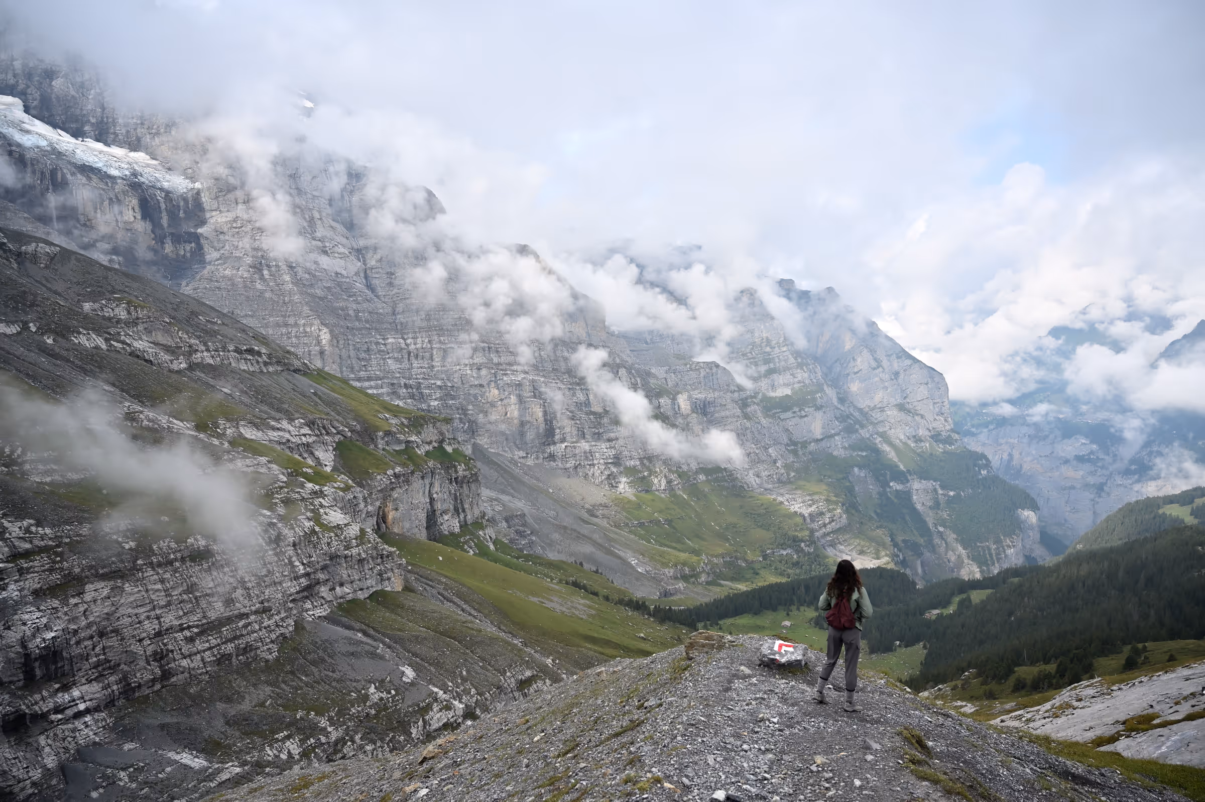 Hiker standing on rocky alpine terrain as mist and low clouds roll through Kleine Scheidegg.