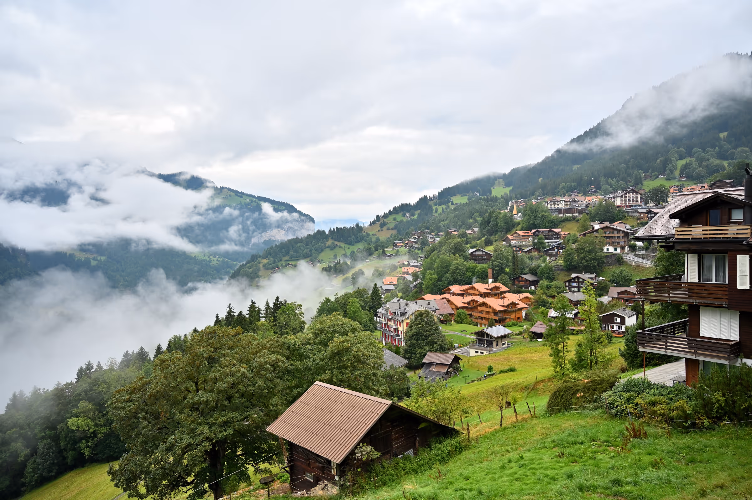 Rolling green hills and alpine homes in Wengen with low clouds moving through the landscape.