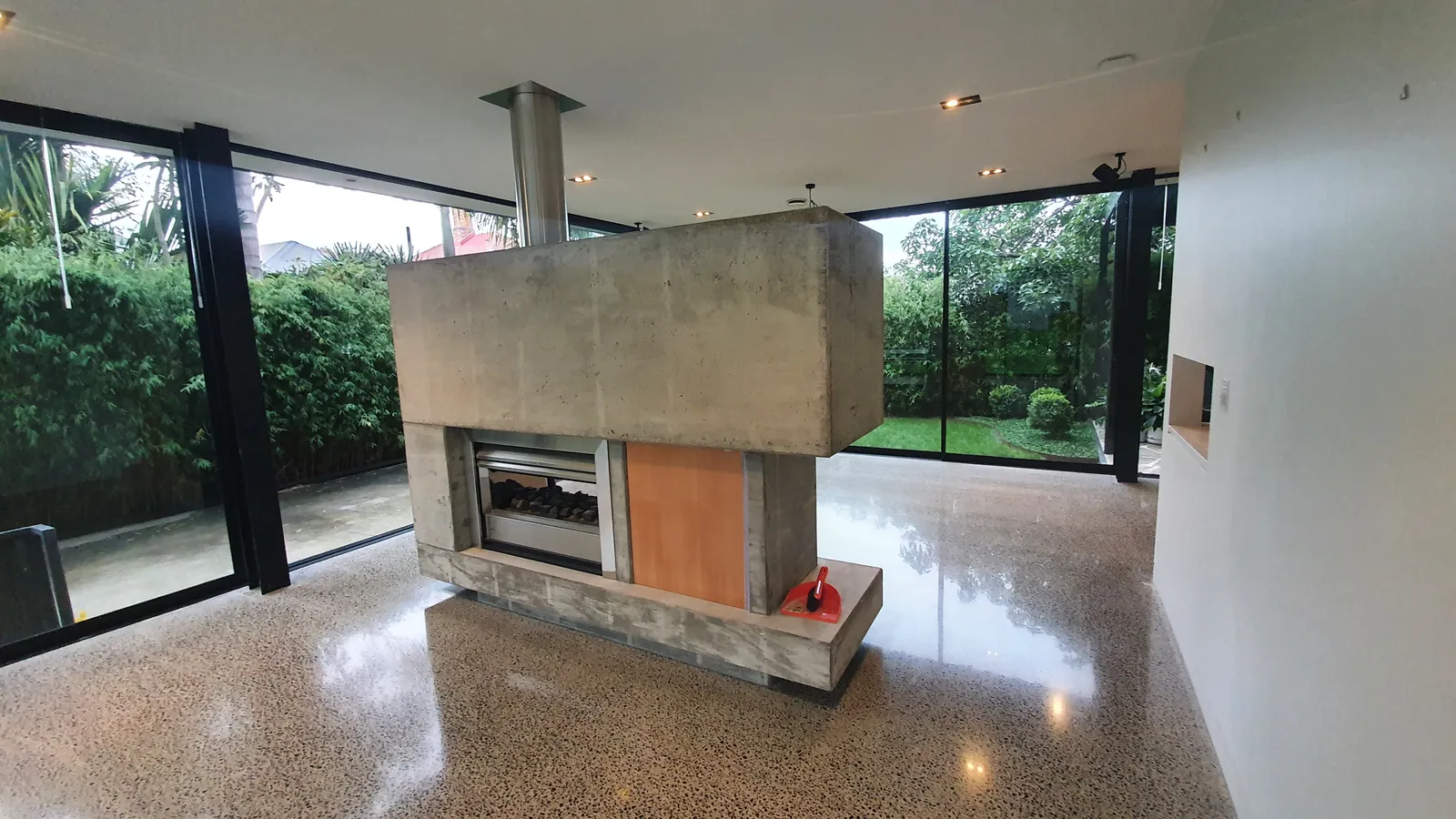Diamond Shine Concrete coloured polished concrete floor in Auckland living room with concrete fireplace and garden views