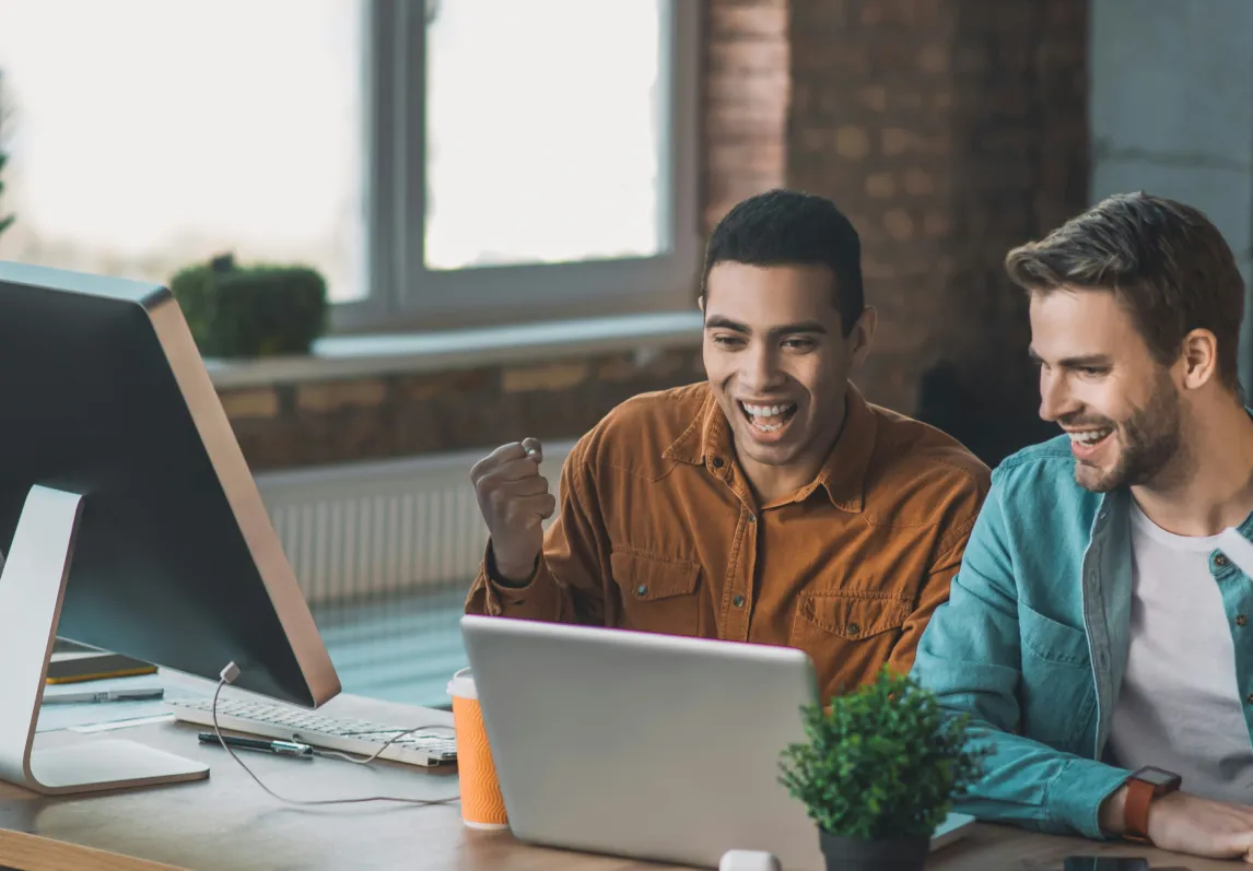 Two men sitting at a desk looking at a computer screen.