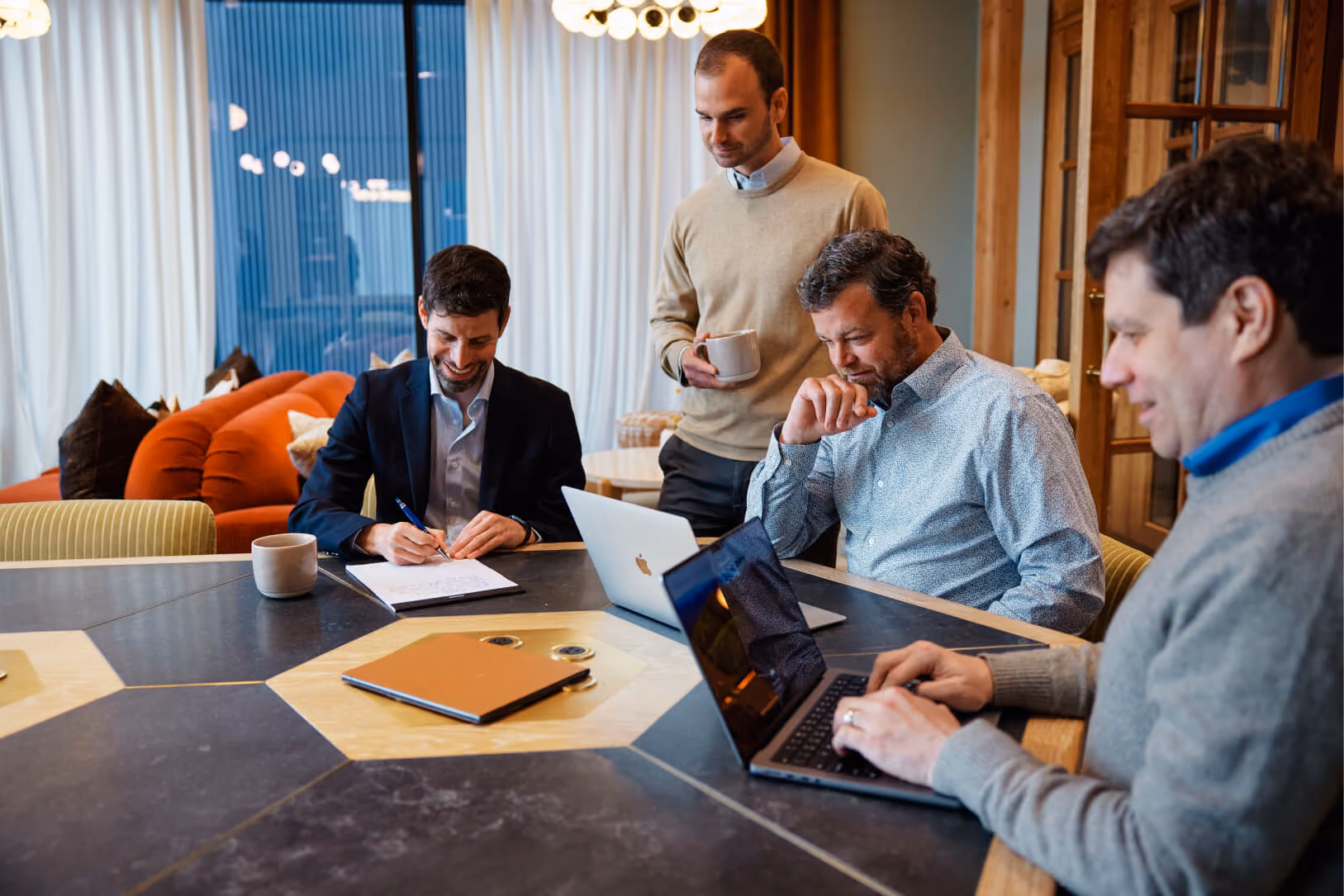Four men sitting around a table, working on their laptops