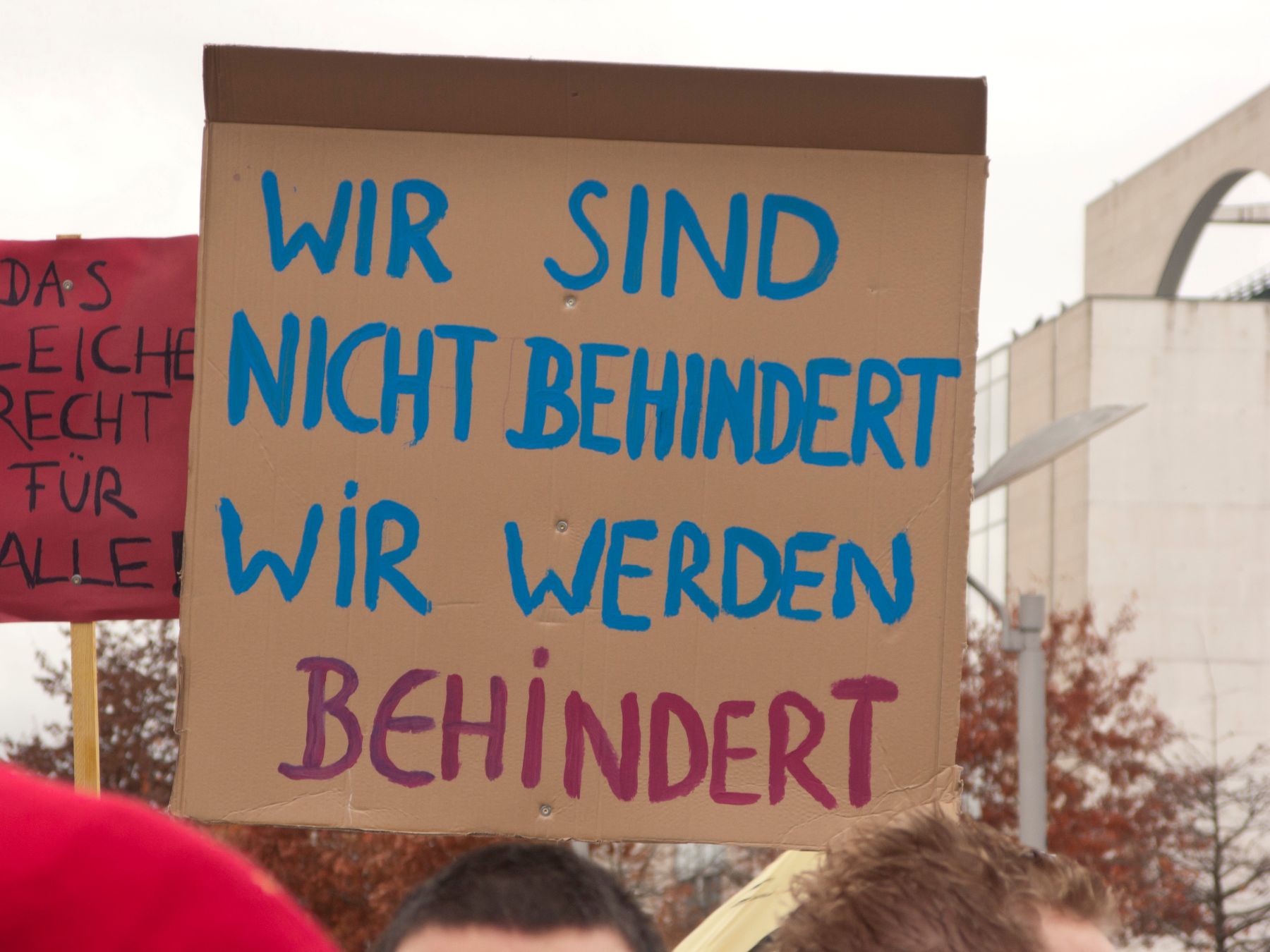 Ein Protestschild wird hochgehalten. Die Aufschrift: "Wir sind nicht behindert! Wir werden behindert."