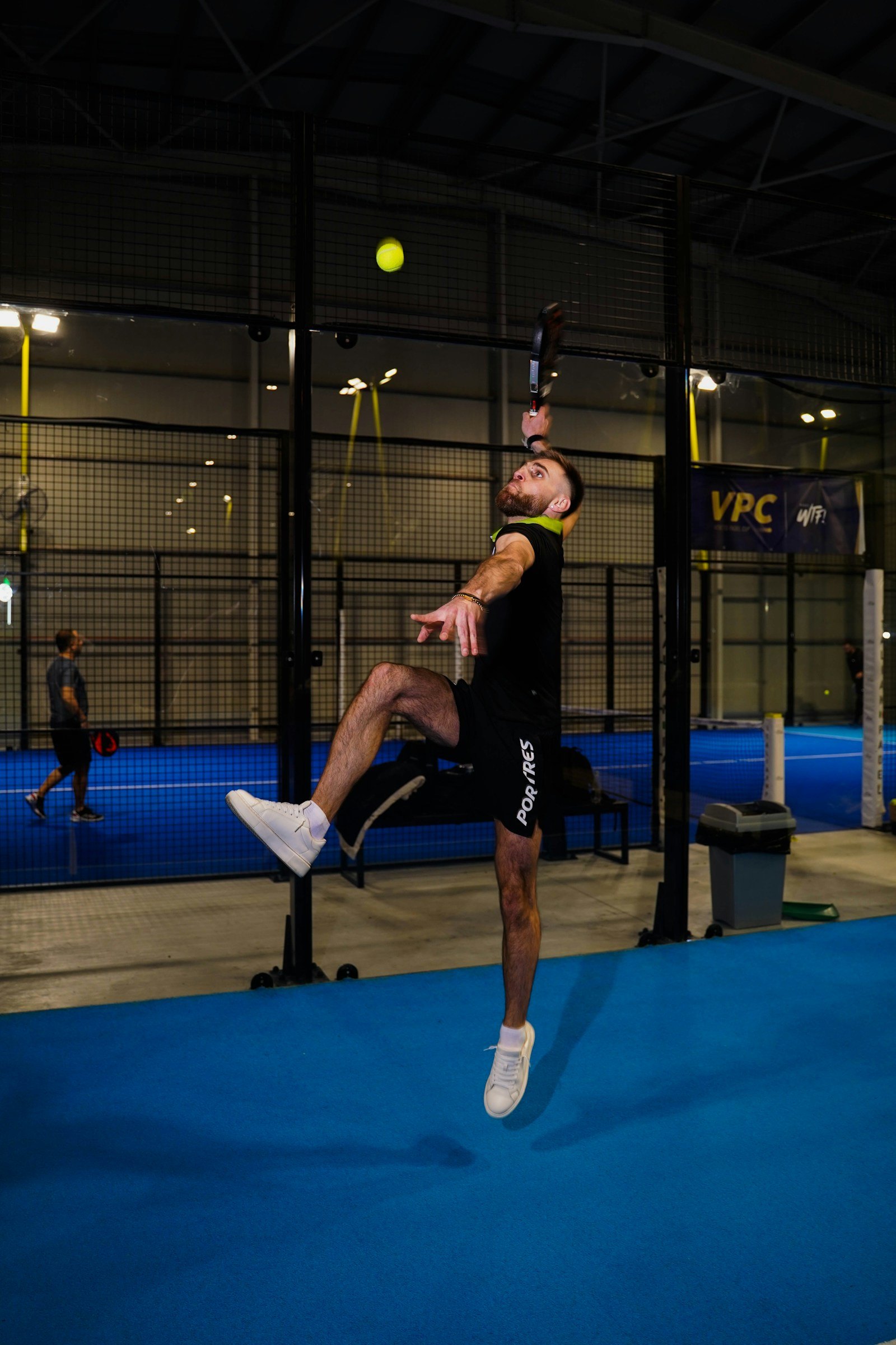 Un joueur de padel saute pour smasher, sur un court bleu couvert